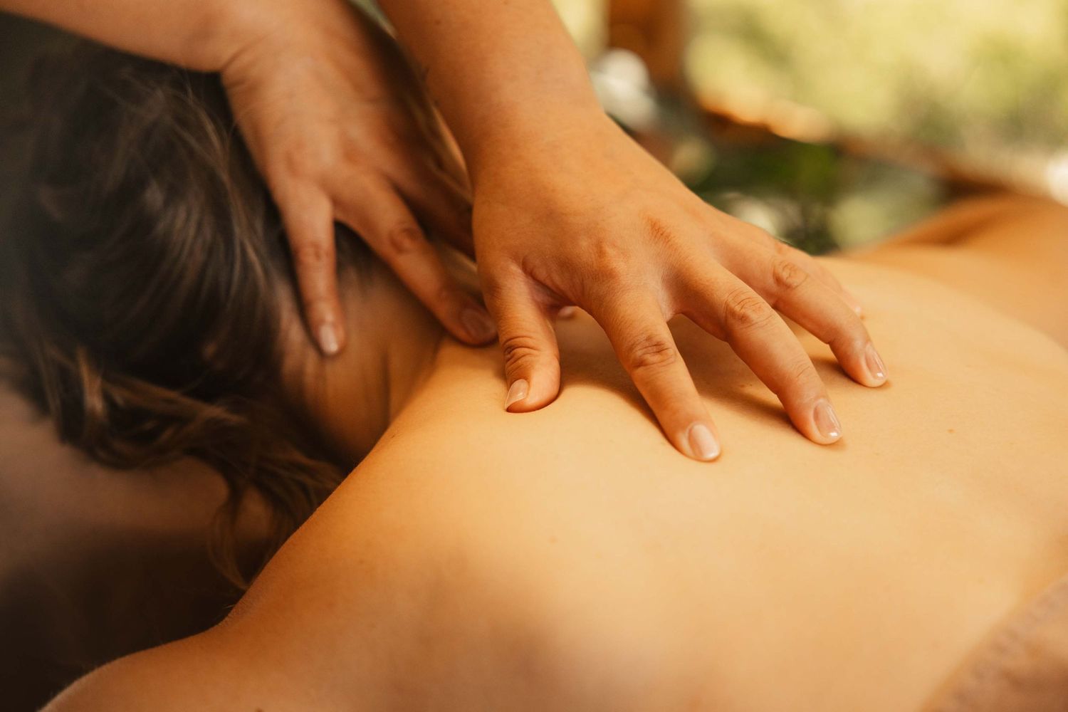 Close-up of a therapist performing a relaxing back massage at a spa with warm, natural lighting.