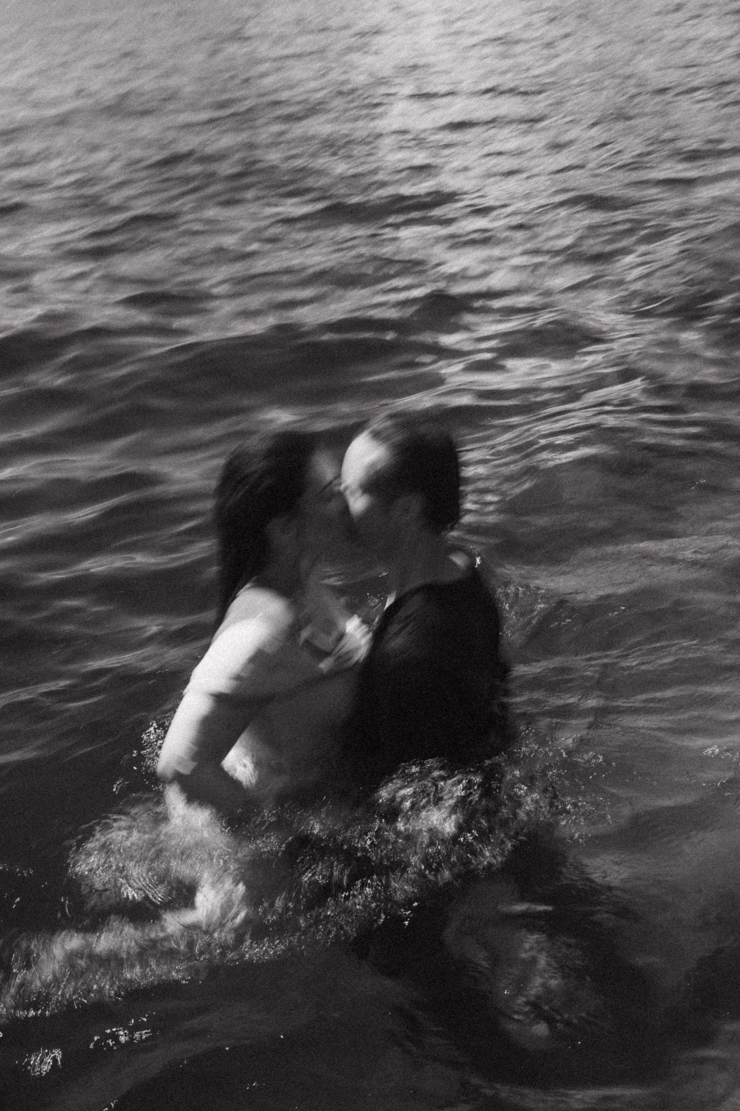 Couple embraces and kisses while swimming in open water, captured in artistic black and white photo.