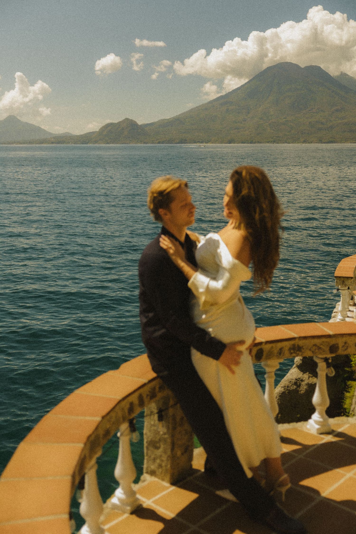 Couple embracing on ornate balcony overlooking Lake Atitlan with volcanic mountains in Guatemala.