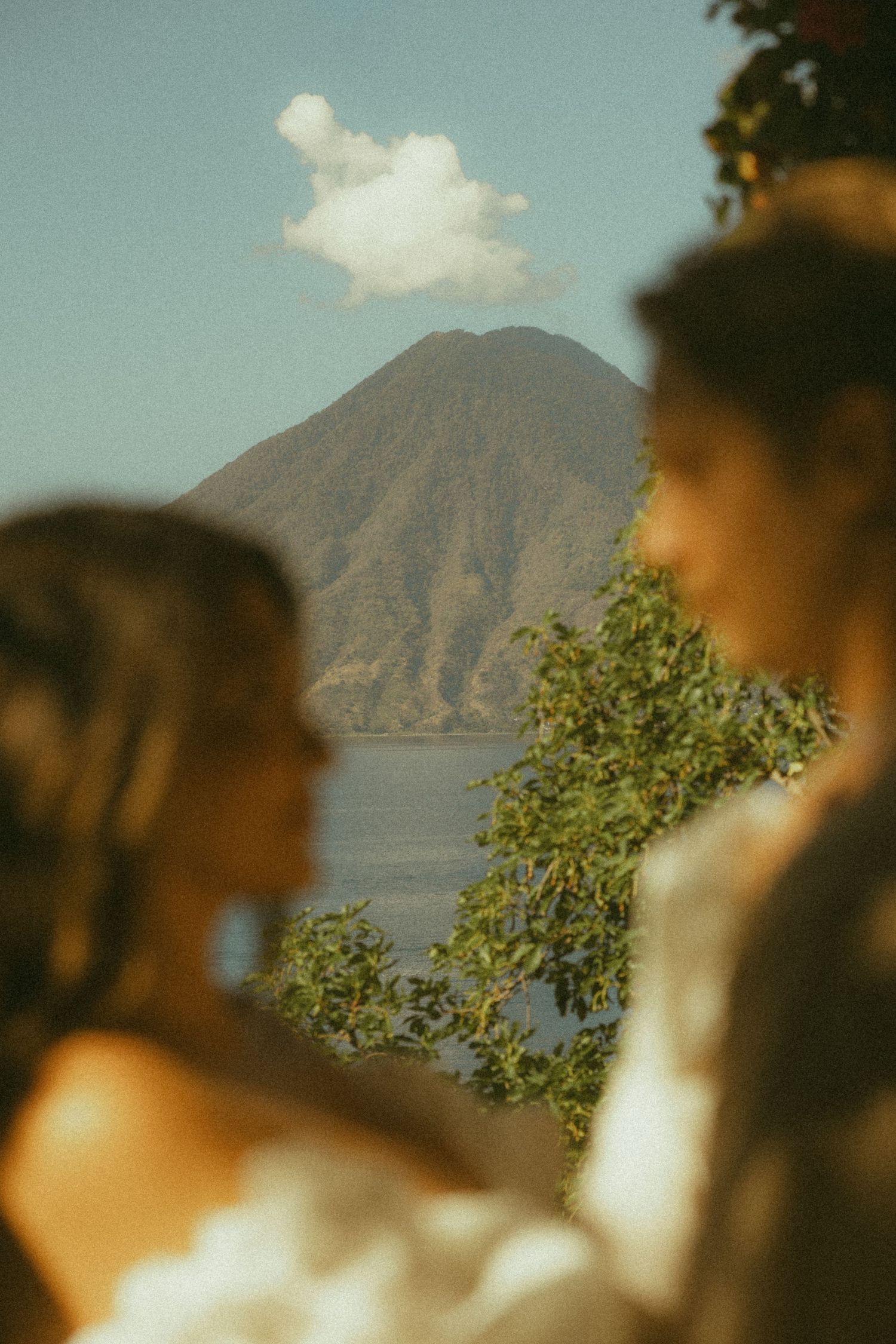 Two brides stand before a stunning volcanic lake landscape on their wedding day.