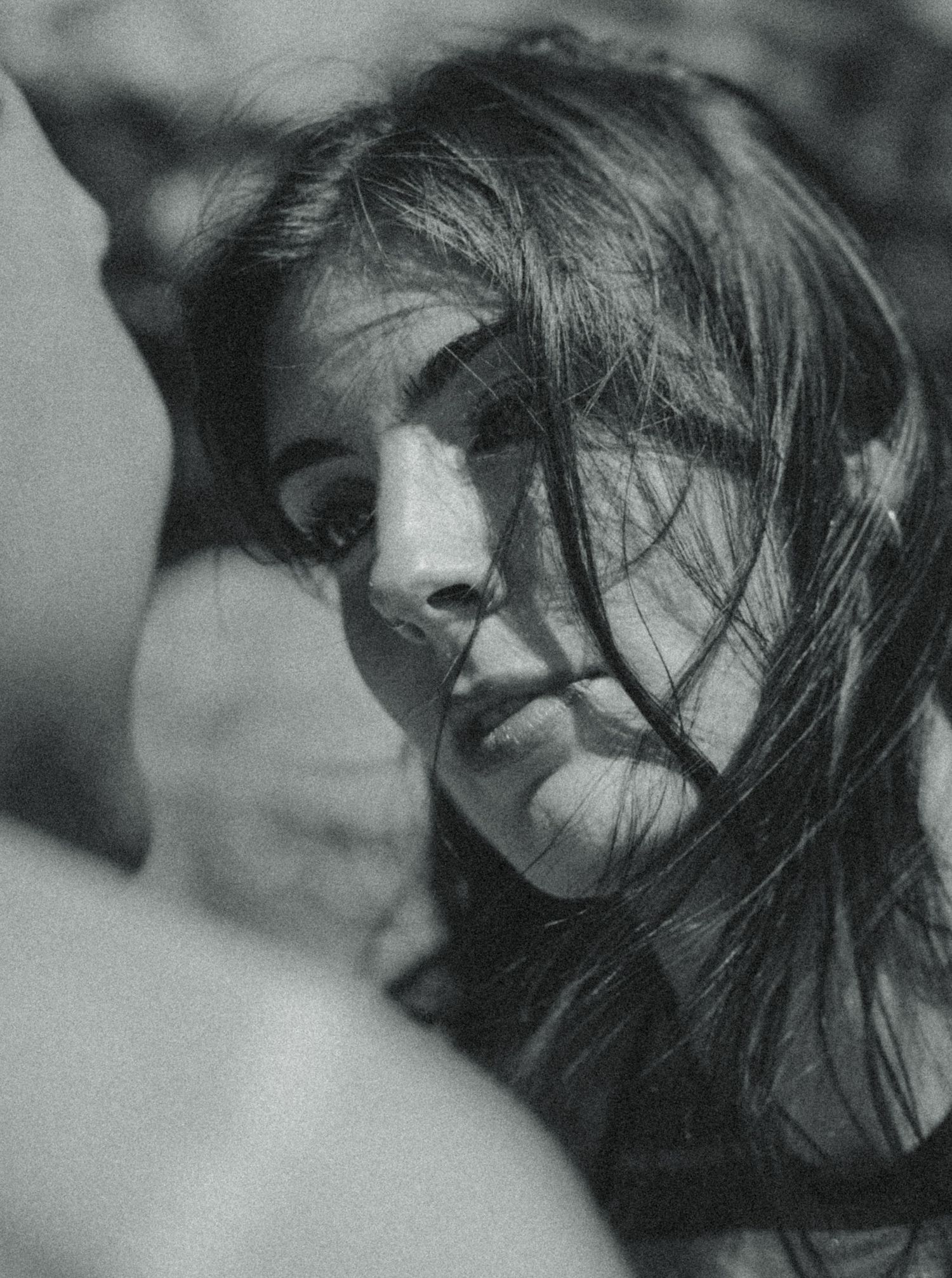 Black and white close-up portrait of a young woman with wind-blown hair, captured in soft natural light.