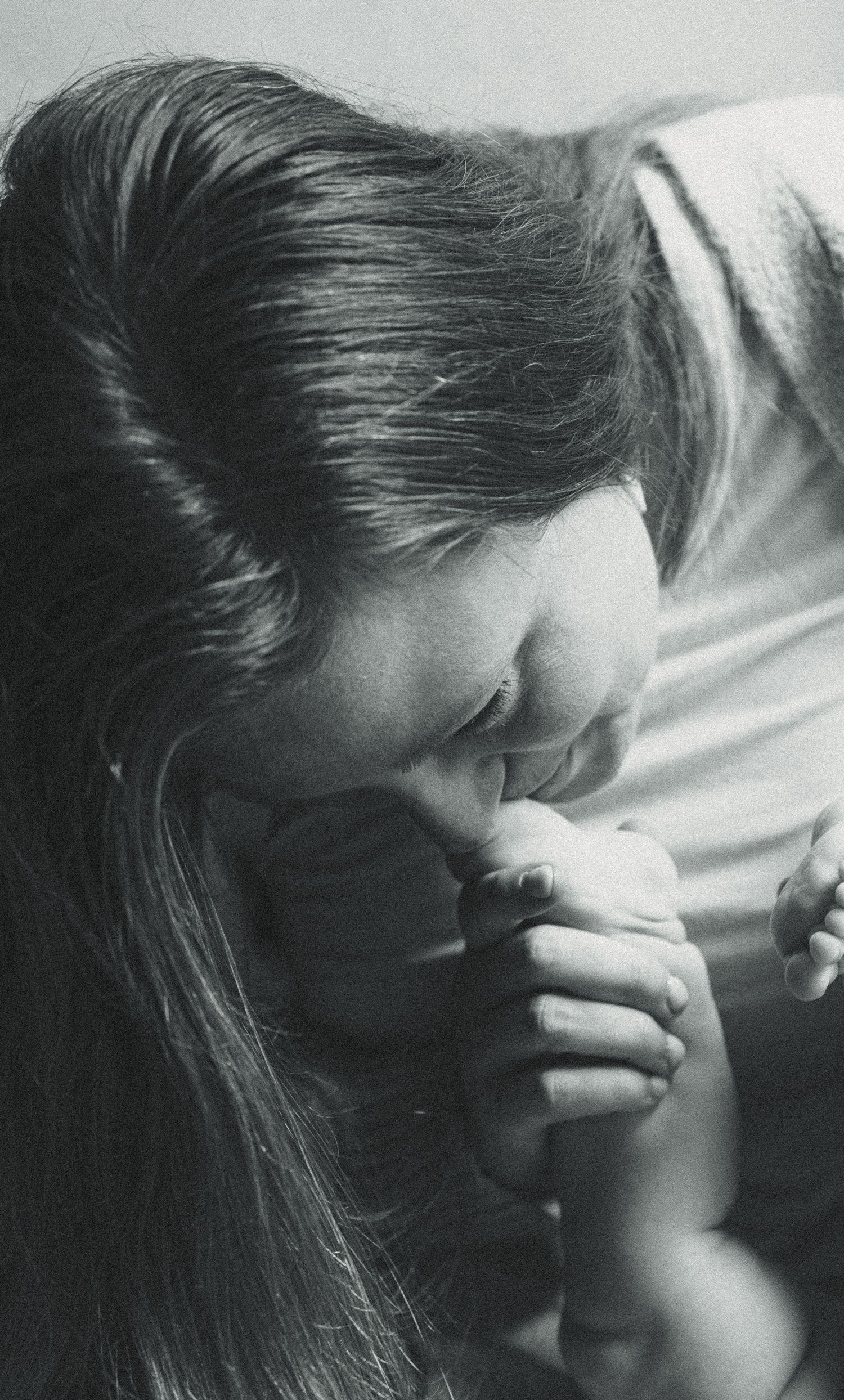 Black and white photo of a woman with long hair bowing her head in prayer, hands clasped together.