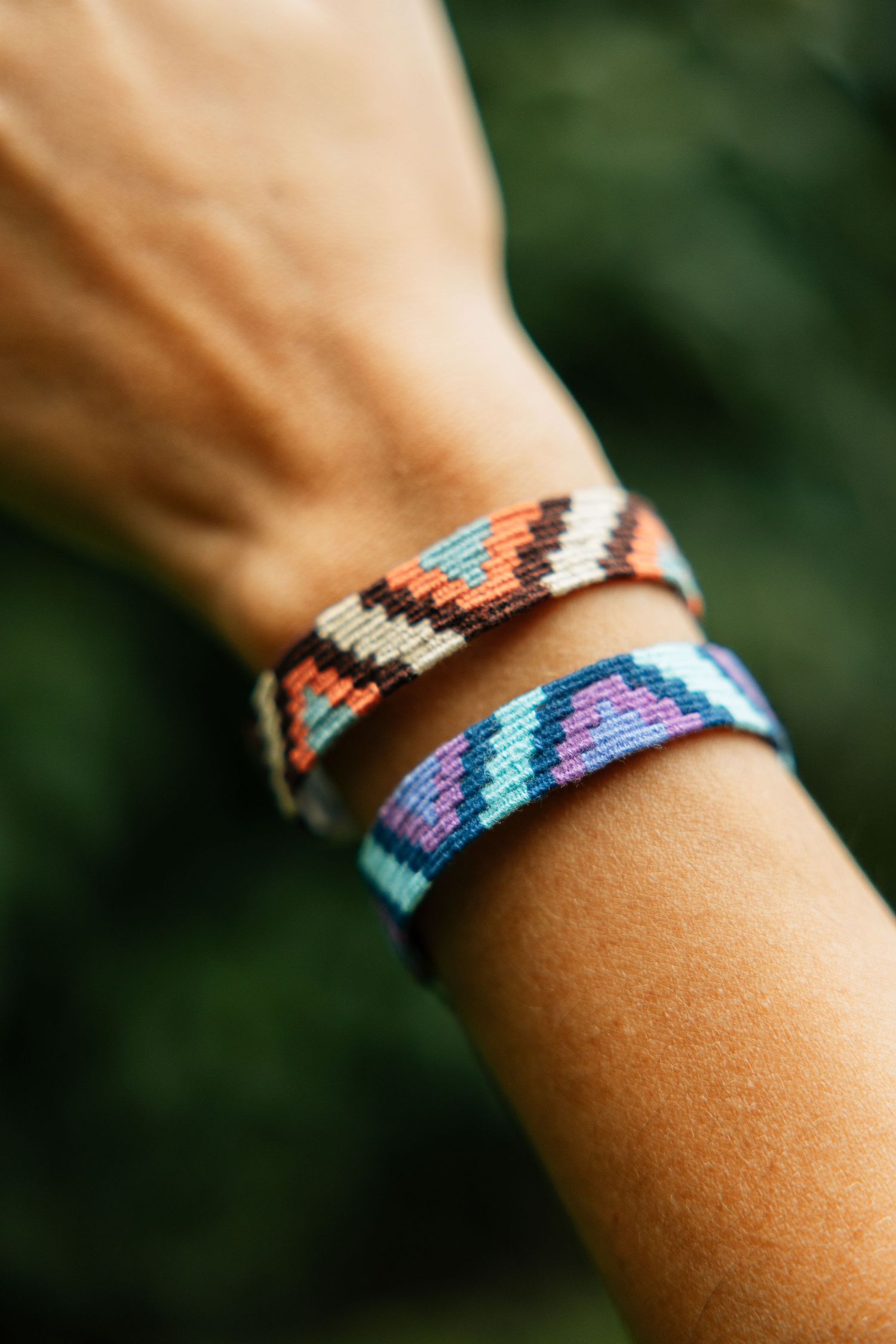 Two colorful woven friendship bracelets with zigzag patterns in orange, blue, and purple on a wrist.
