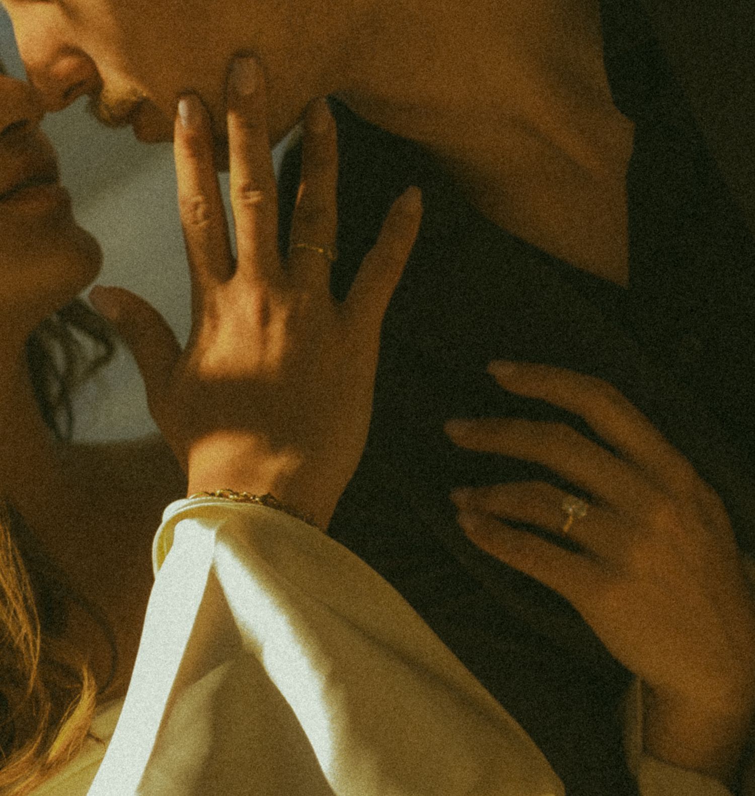 Close-up of brides hand with engagement ring and bracelet resting on grooms dark jacket.