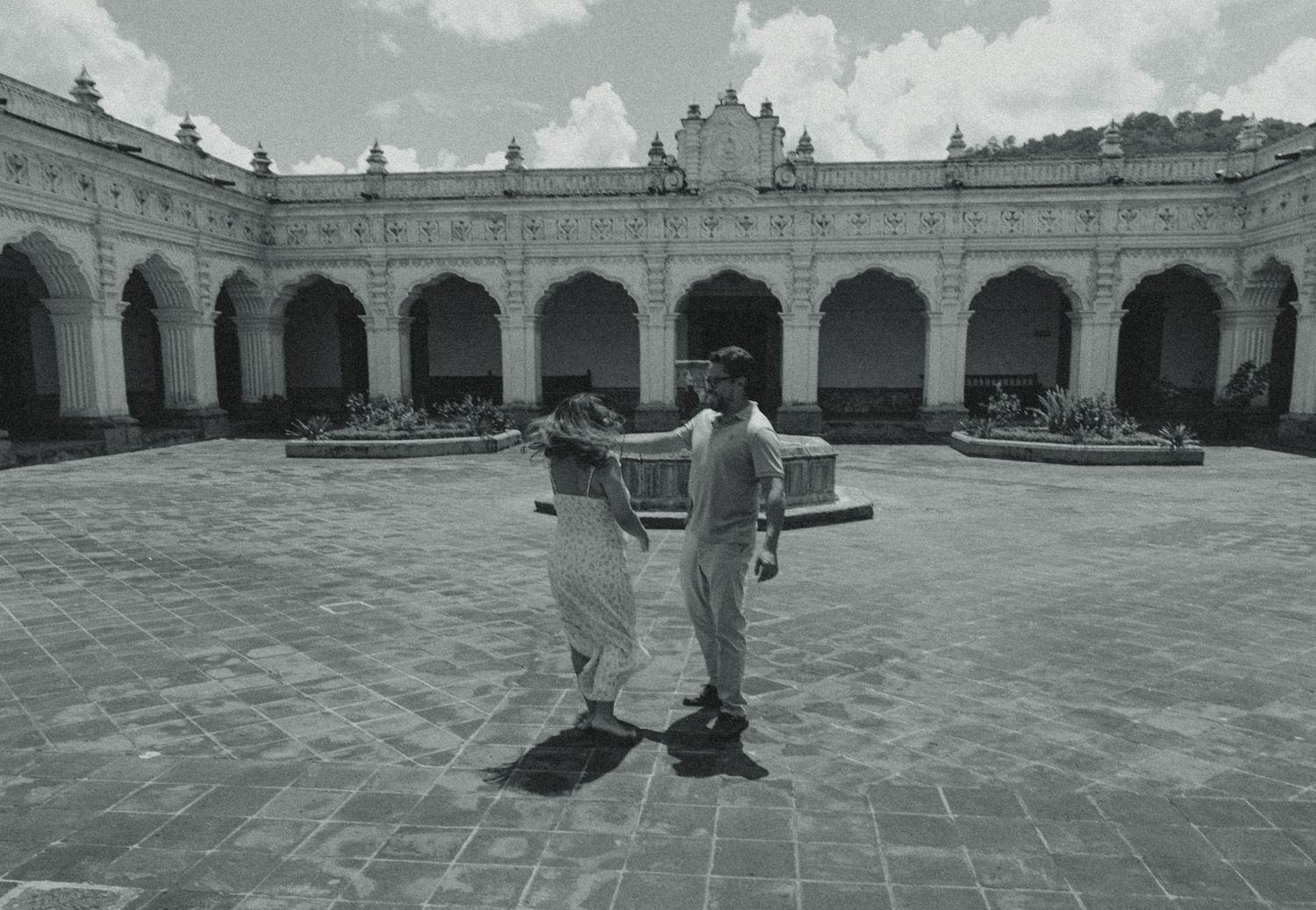 Two people stand in a grand colonial courtyard with arched colonnades in a black and white photo.