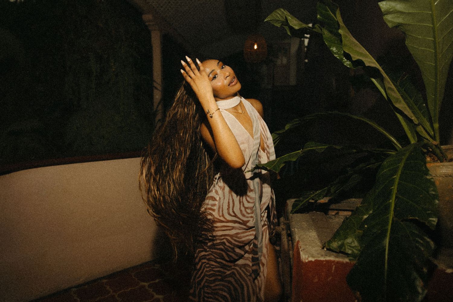 Woman in zebra print dress poses dramatically among tropical plants in warm evening light.