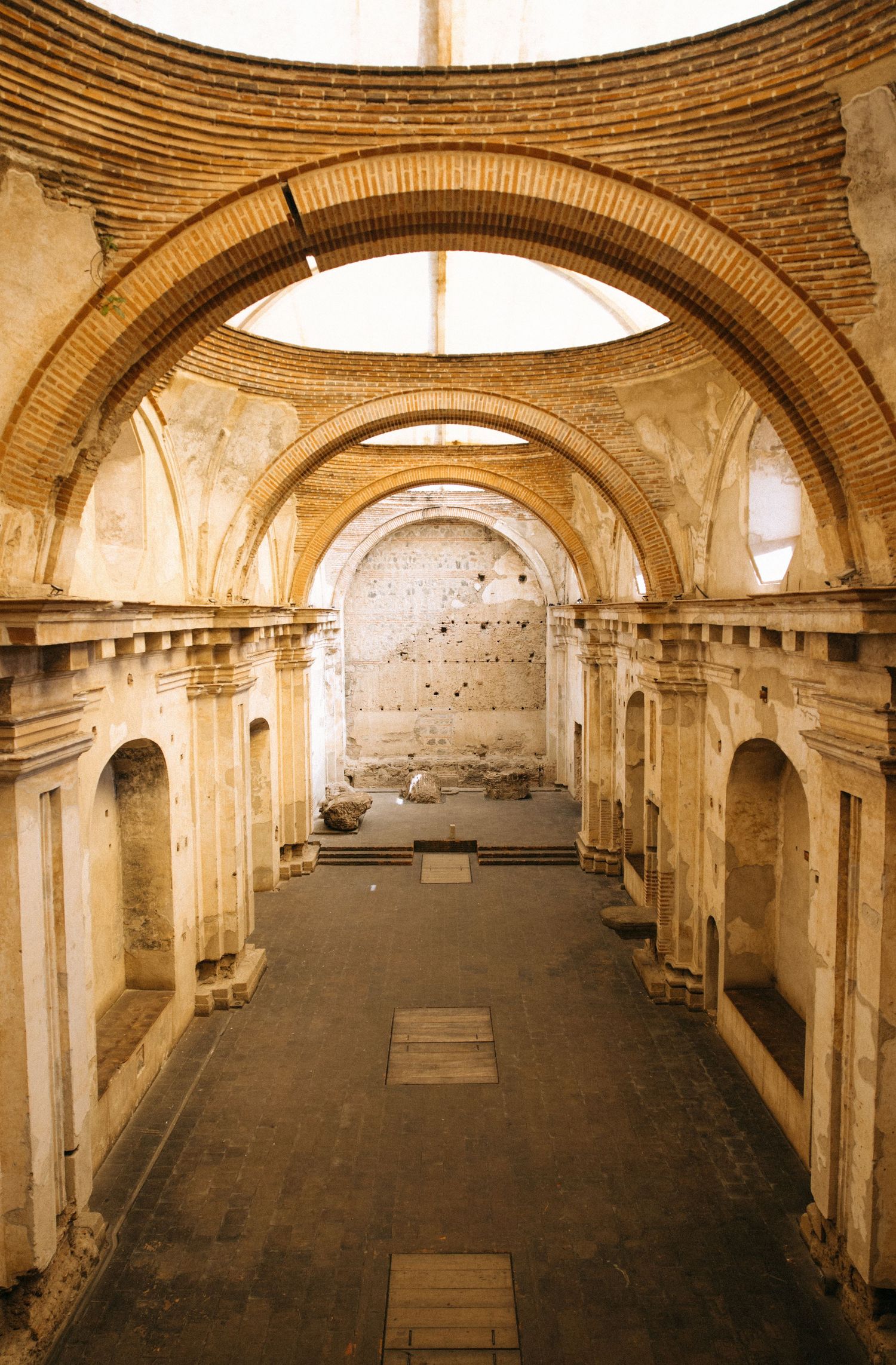 Ruined colonial church interior with brick arches, weathered stone walls and an open roof letting daylight onto the worn floor.