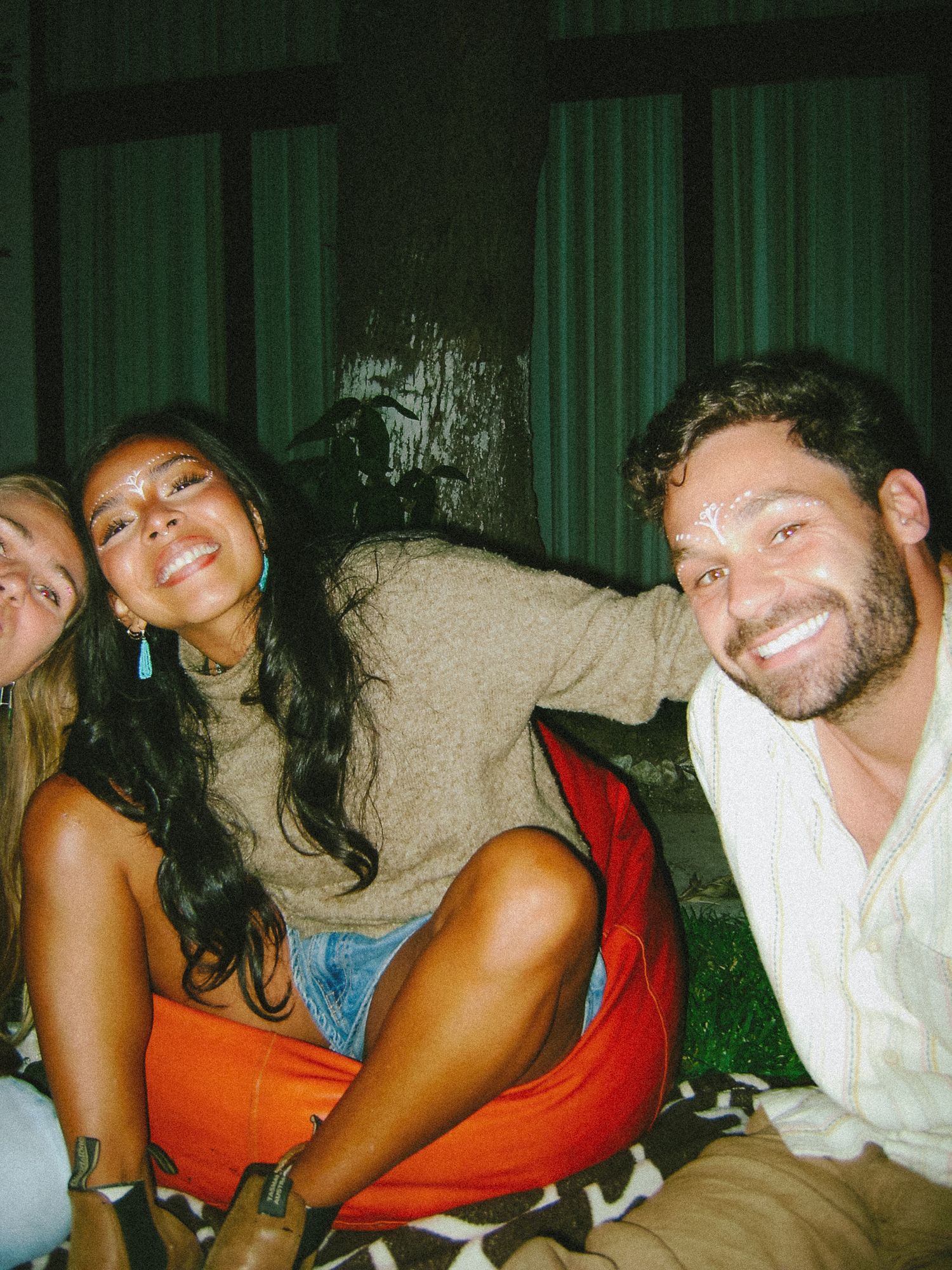Three friends smiling and posing together outdoors at night, sitting casually on the ground.