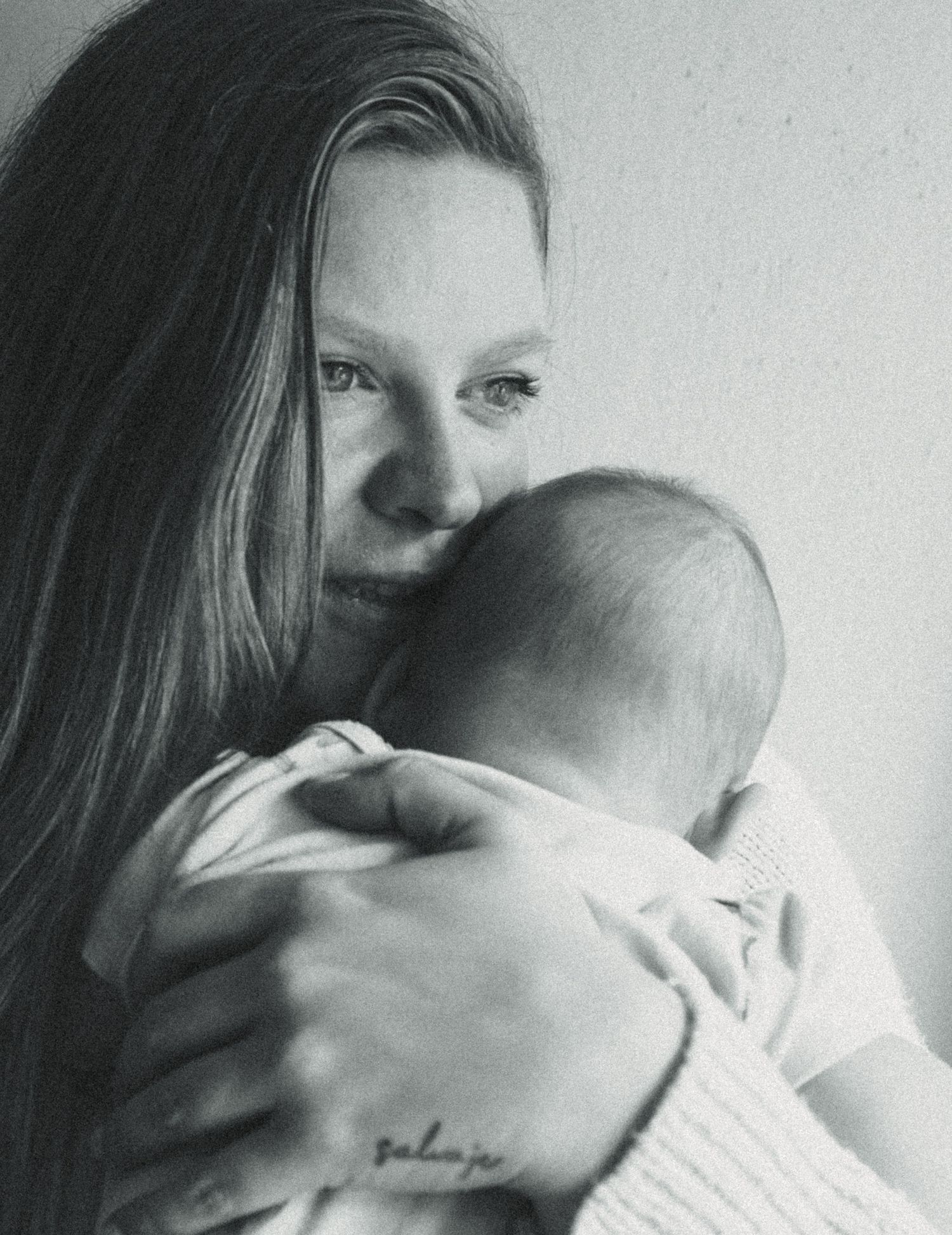 Black and white photo of a young mother tenderly holding and nuzzling her newborn baby close to her chest.