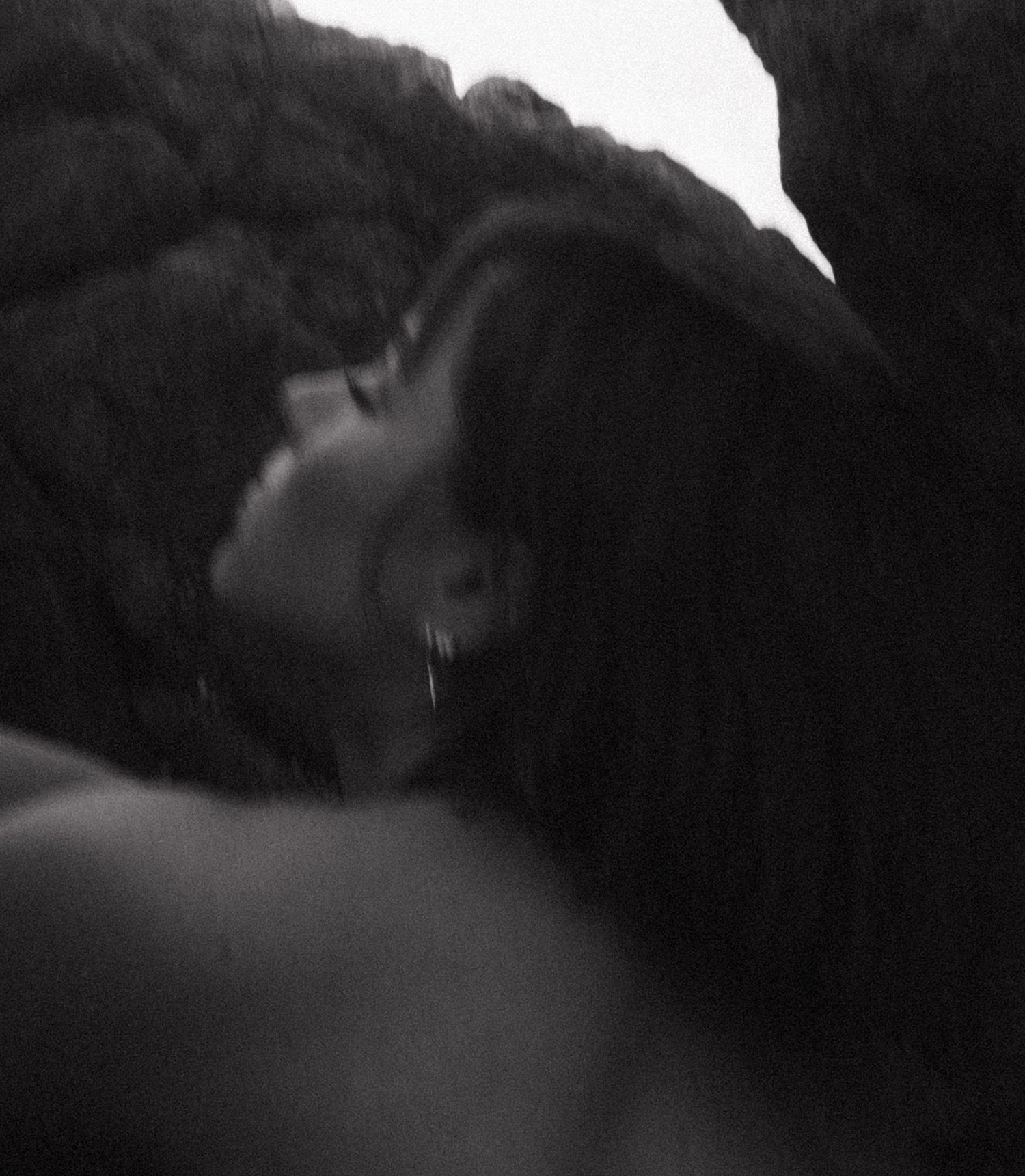 Black and white photo of two people sharing a romantic kiss in a dimly lit, intimate setting.