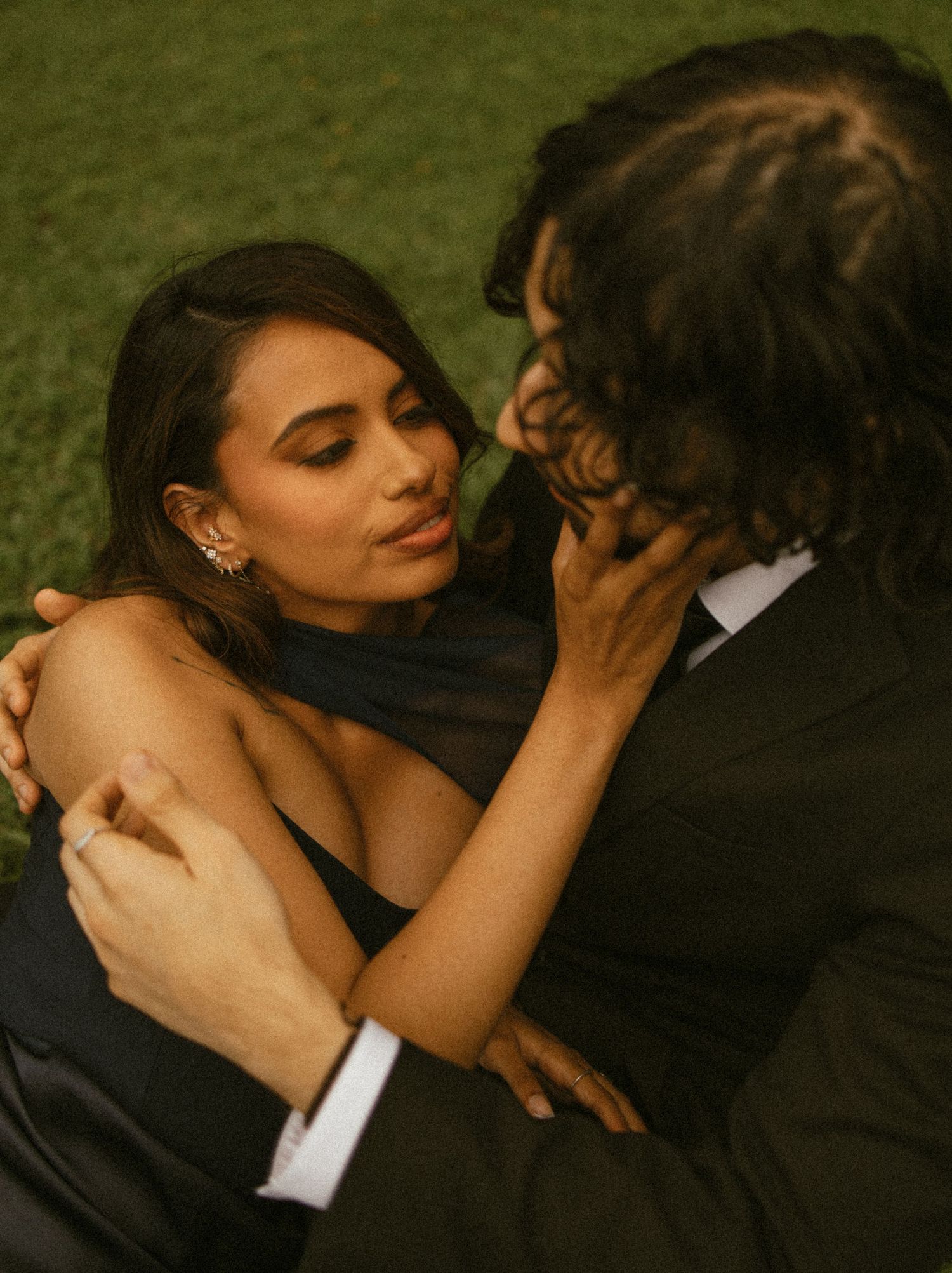 Couple in formal attire sharing an intimate moment outdoors, woman in black dress embracing man in suit.