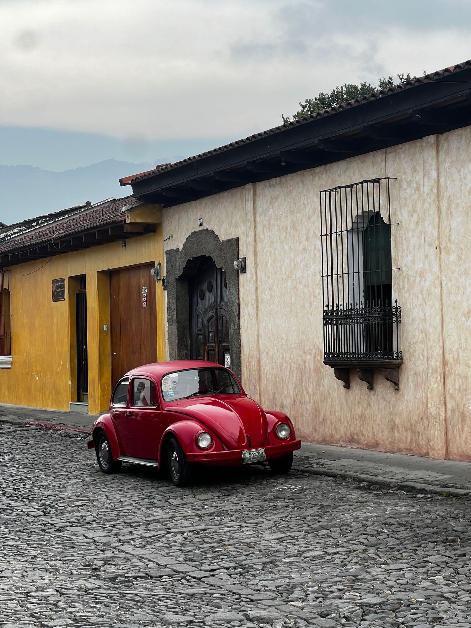 Red VW Beetle parked on cobblestone street in Antigua Guatemala with colorful colonial buildings.