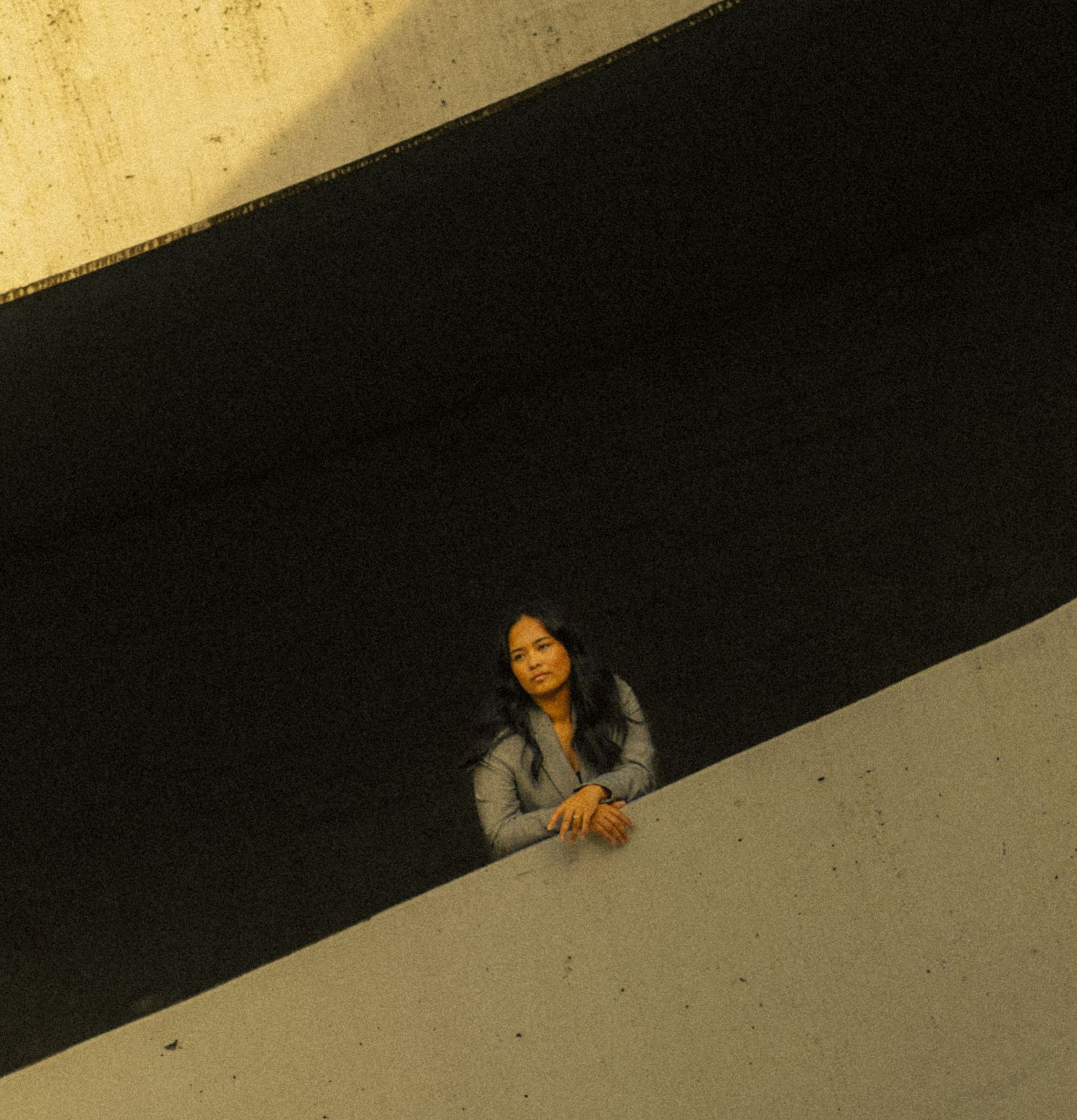 Woman leaning on a concrete ledge between two diagonal architectural lines in warm evening light.