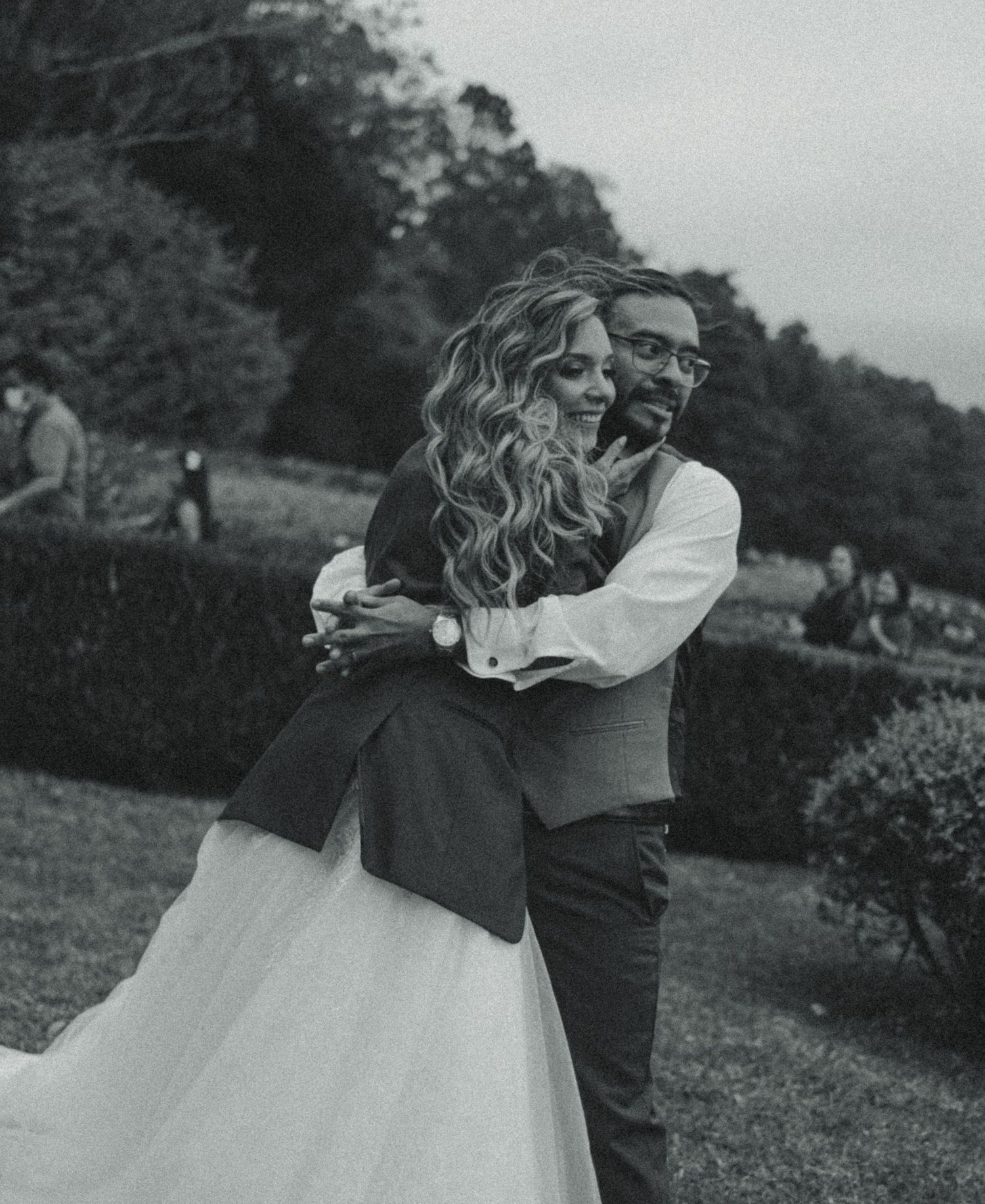 Black and white photo of a bride and groom embracing joyfully outdoors on their wedding day.