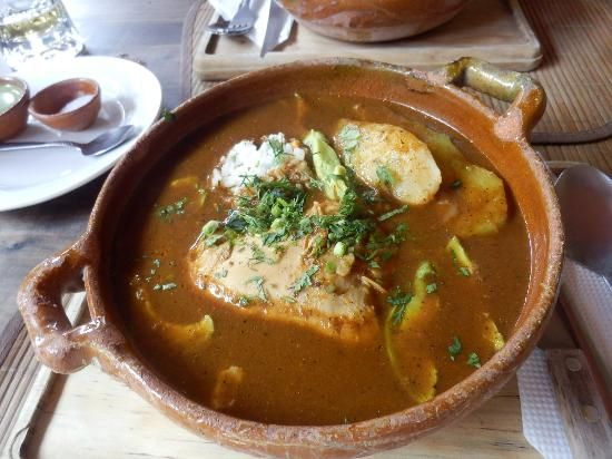 A rustic clay bowl filled with rich Mexican fish stew in savory broth, garnished with fresh herbs and vegetables.