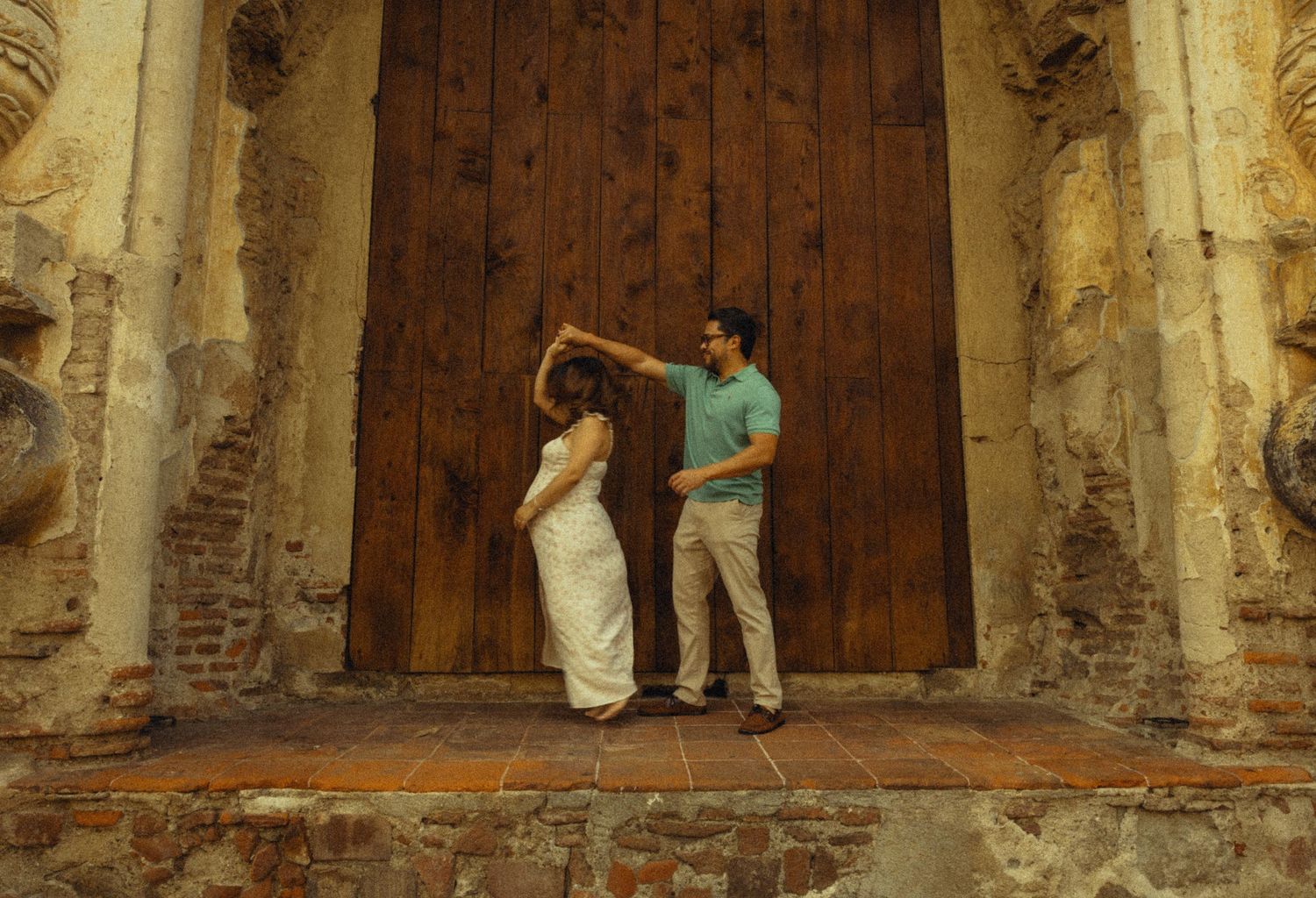 Couple dancing elegantly in front of a rustic wooden door at a historic stone building.