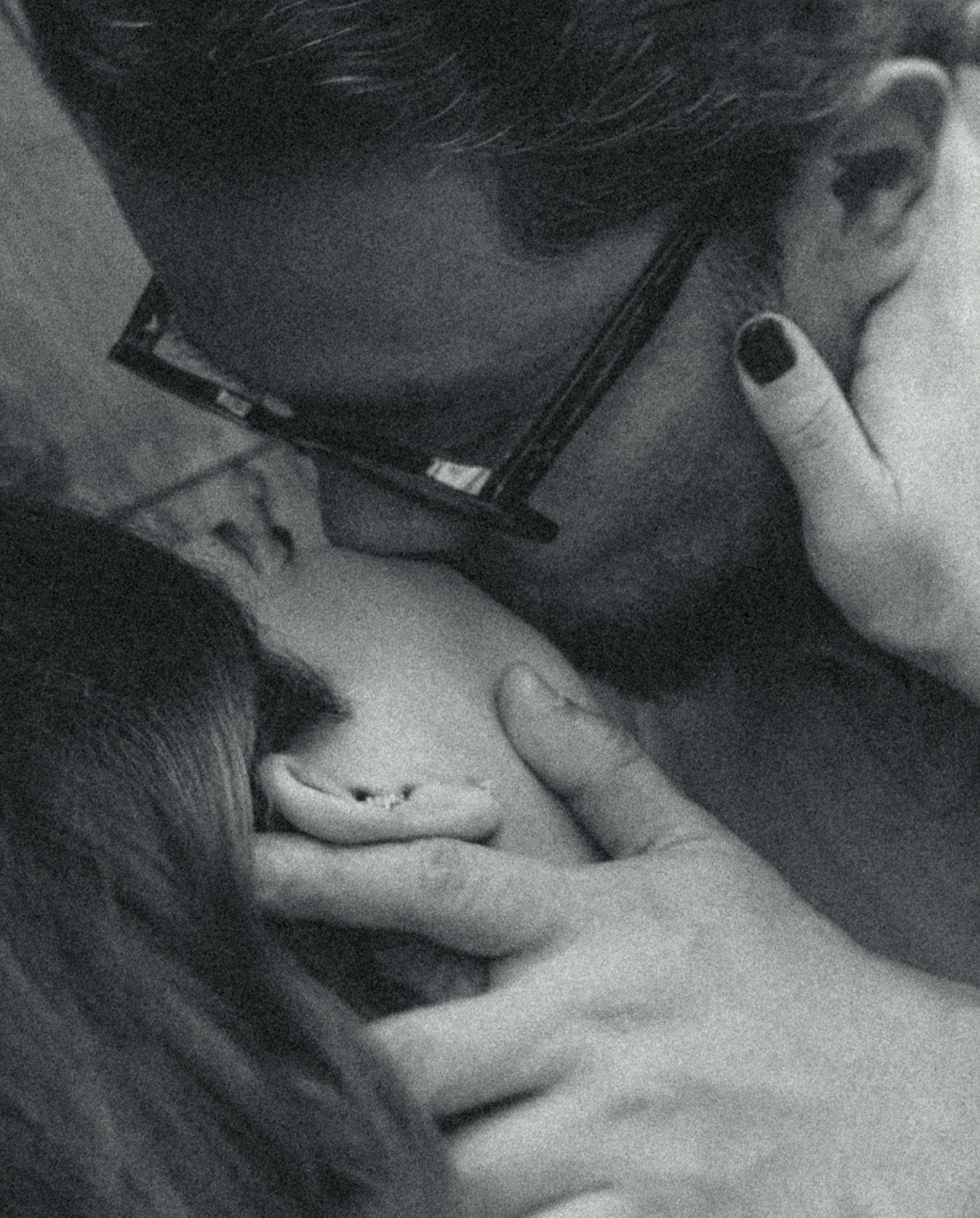Black and white photo of a couple sharing an intimate moment, man with glasses gently kissing a woman.