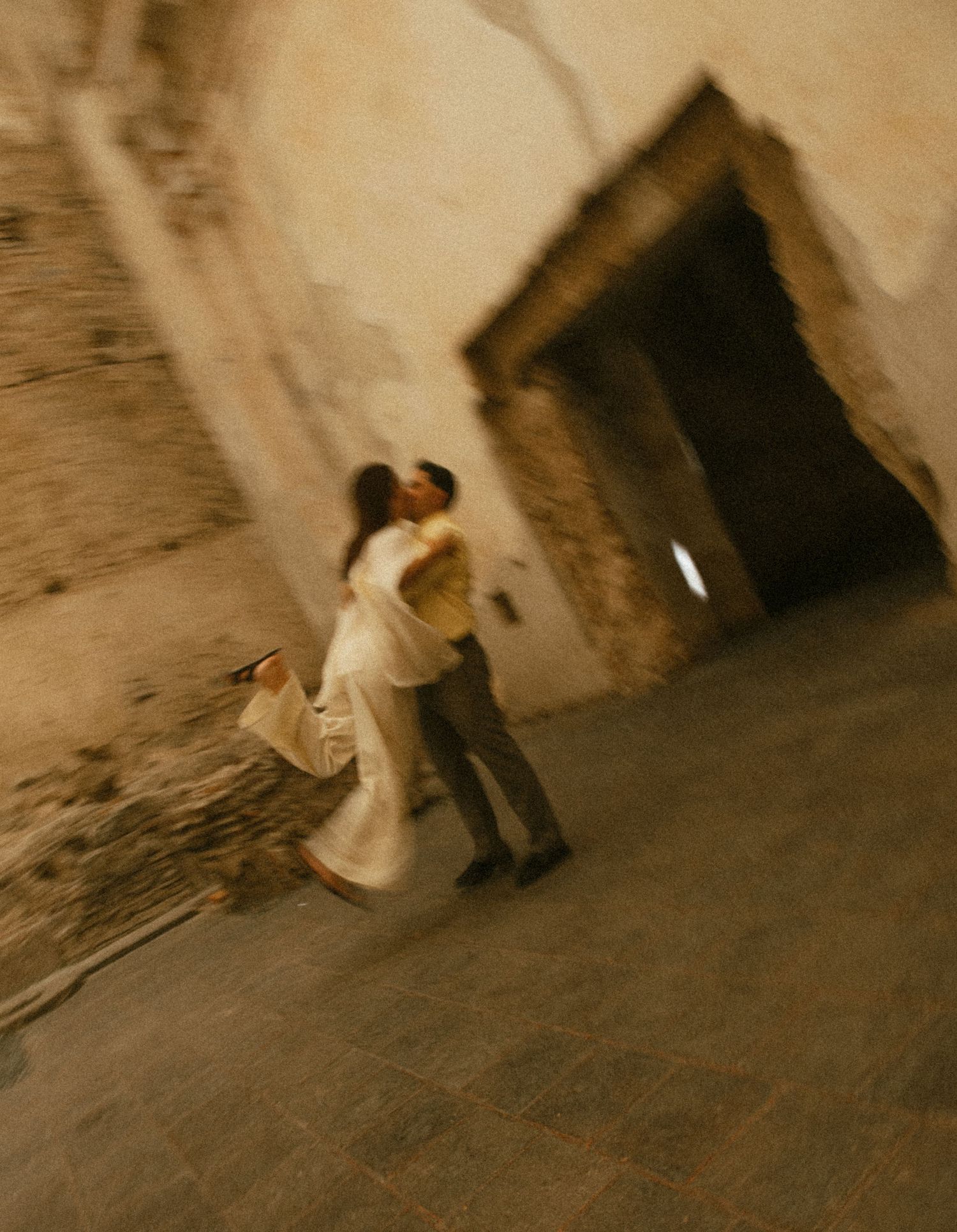 Couple sharing a romantic kiss in a dimly lit ancient stone corridor during their engagement session.