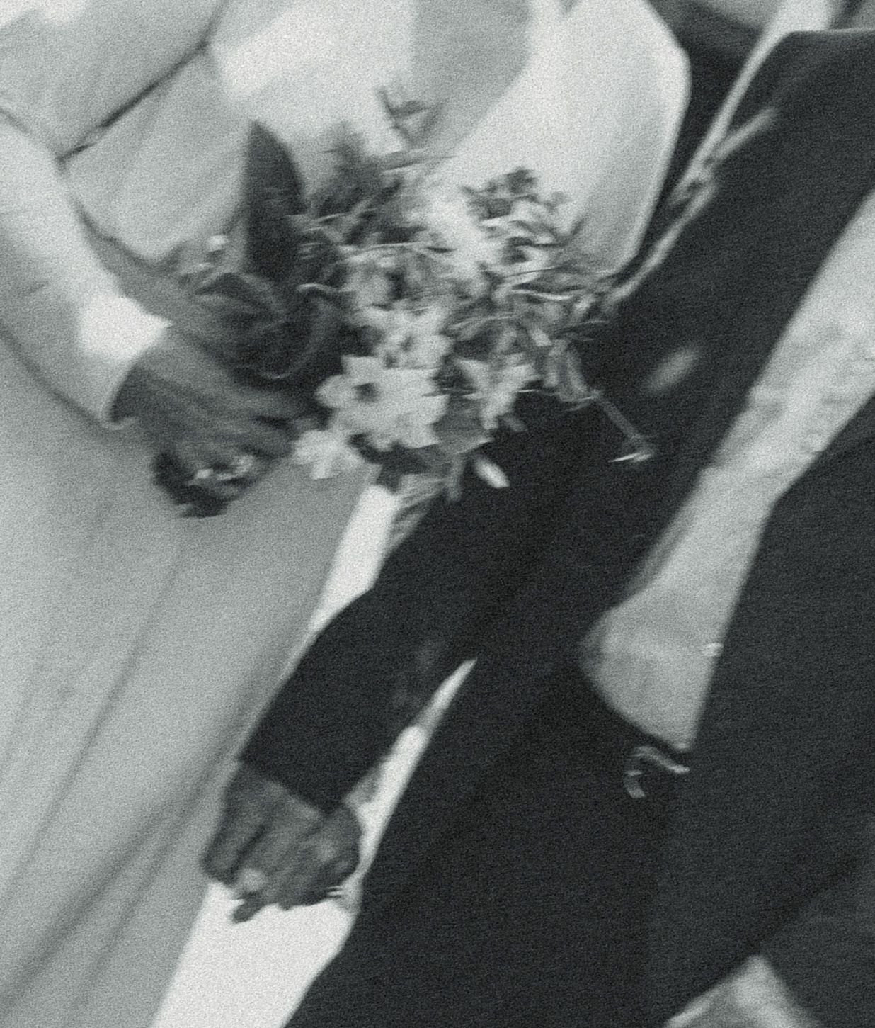Black and white vintage wedding photo of bride holding floral bouquet and groom holding hands in formal attire.