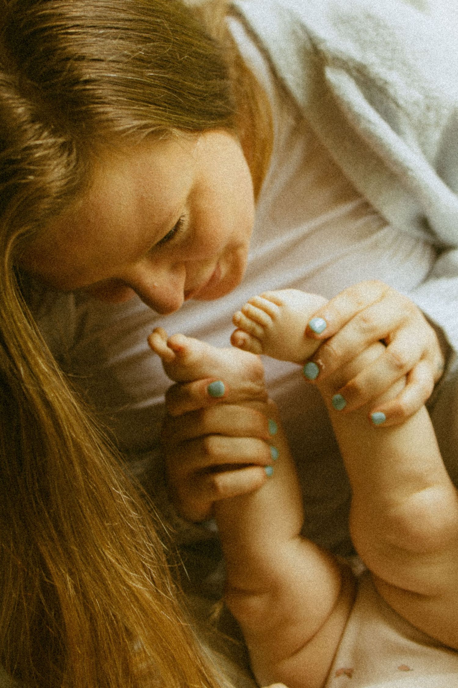 A mother with long hair tenderly kisses her newborn baby's tiny feet while holding them gently.