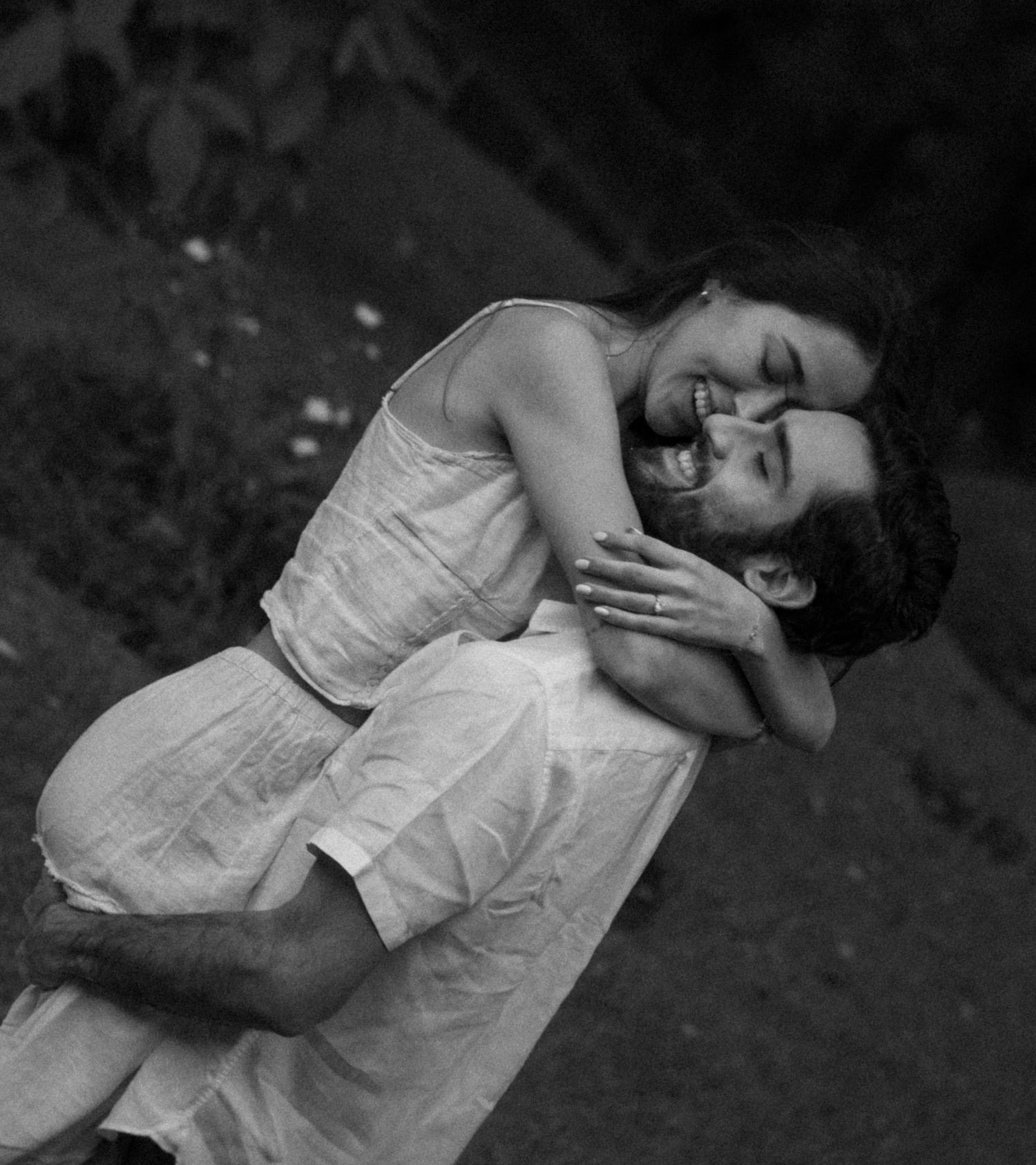 Black and white photo of a couple embracing joyfully outdoors, man lifting woman as they smile and laugh together.