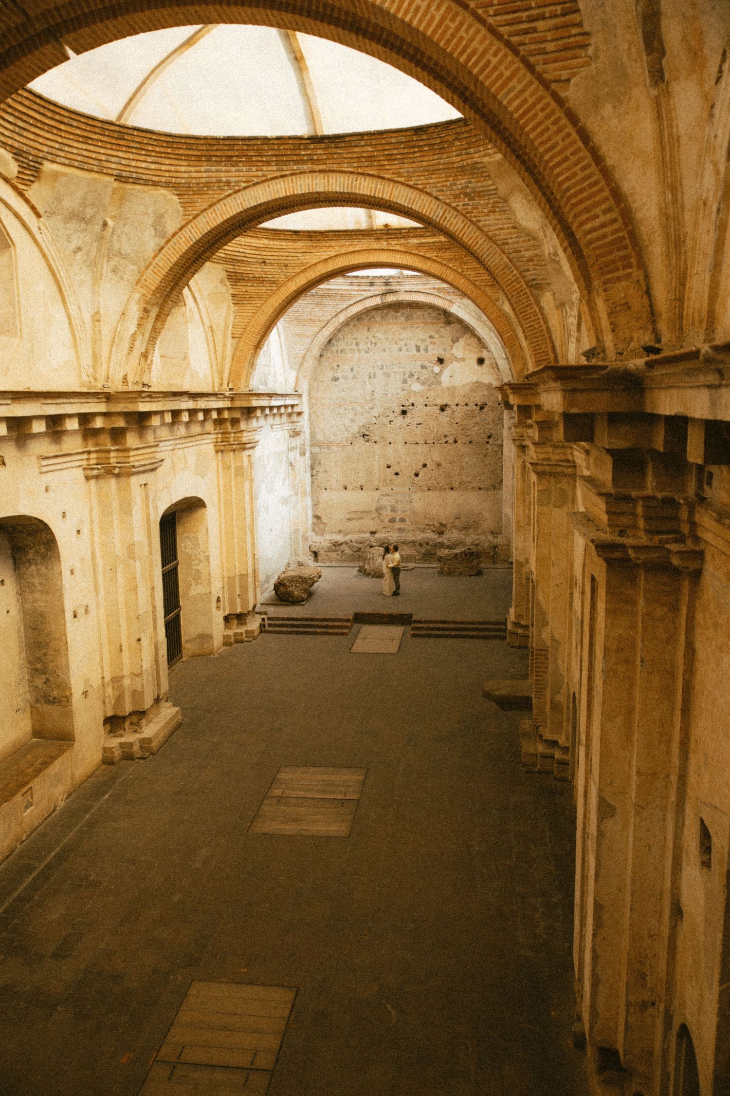 Interior of a ruined colonial cathedral with weathered brick arches, an open domed ceiling, and visitors standing in the stone-floored nave.