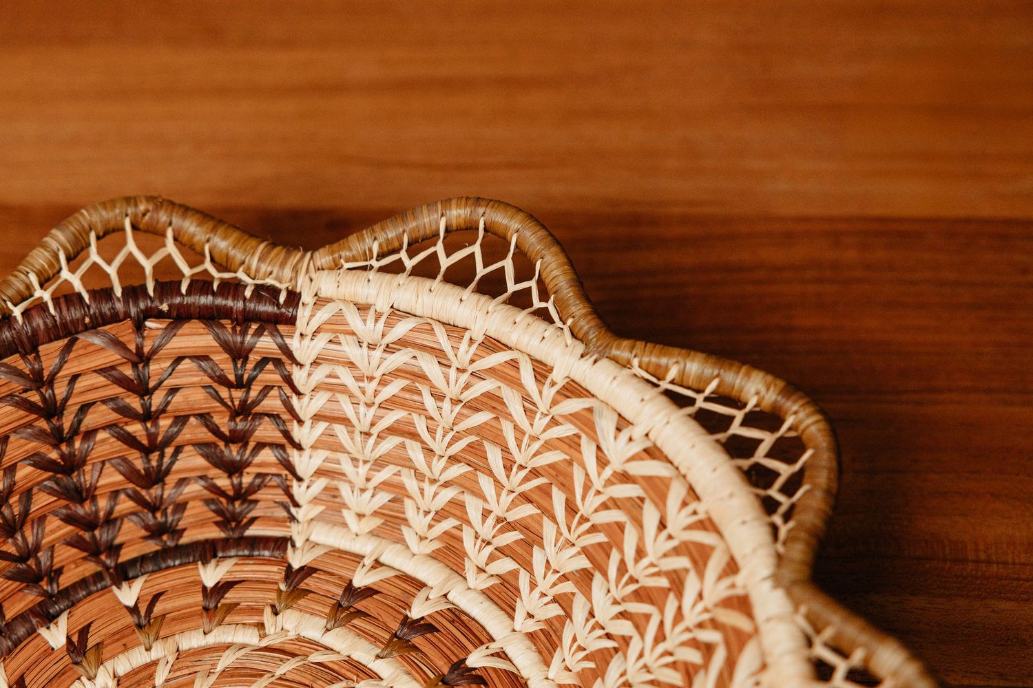 Close-up of a handwoven wicker basket with intricate herringbone pattern and scalloped edges on wooden surface.