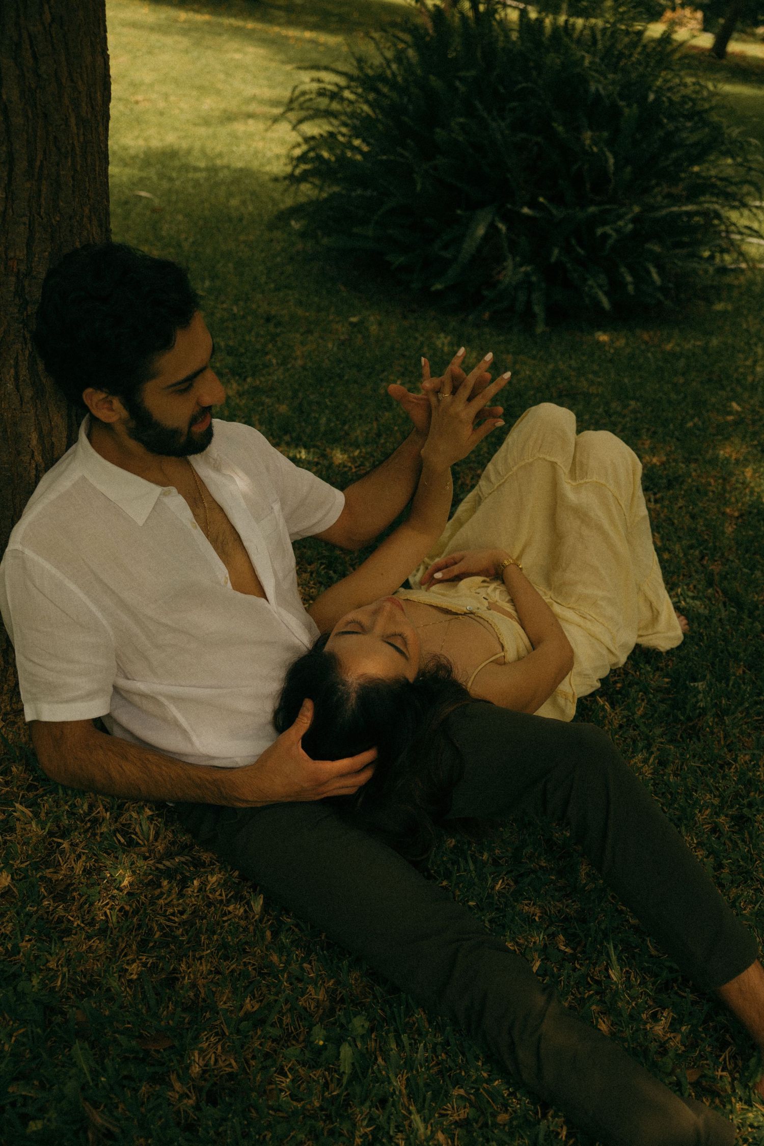 Romantic couple relaxing under a tree, woman lying in mans lap in a sunlit park.