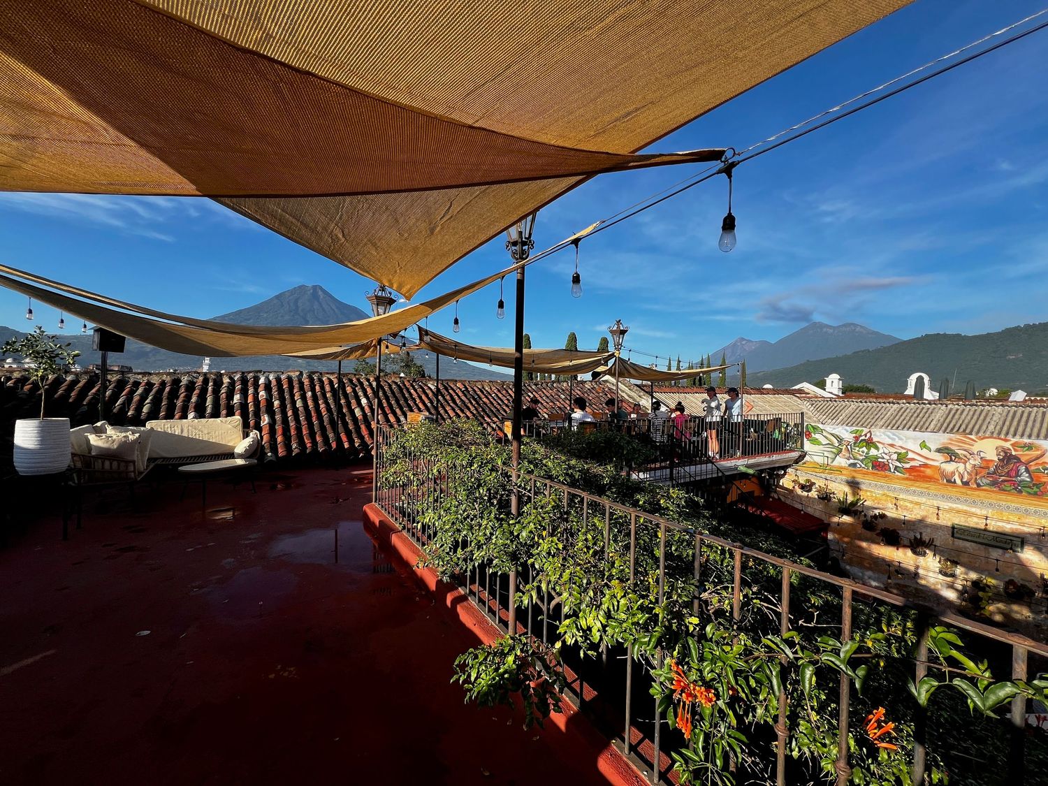 Rooftop terrace with shade sails, lush plants, and stunning volcanic mountain views under a clear blue sky.