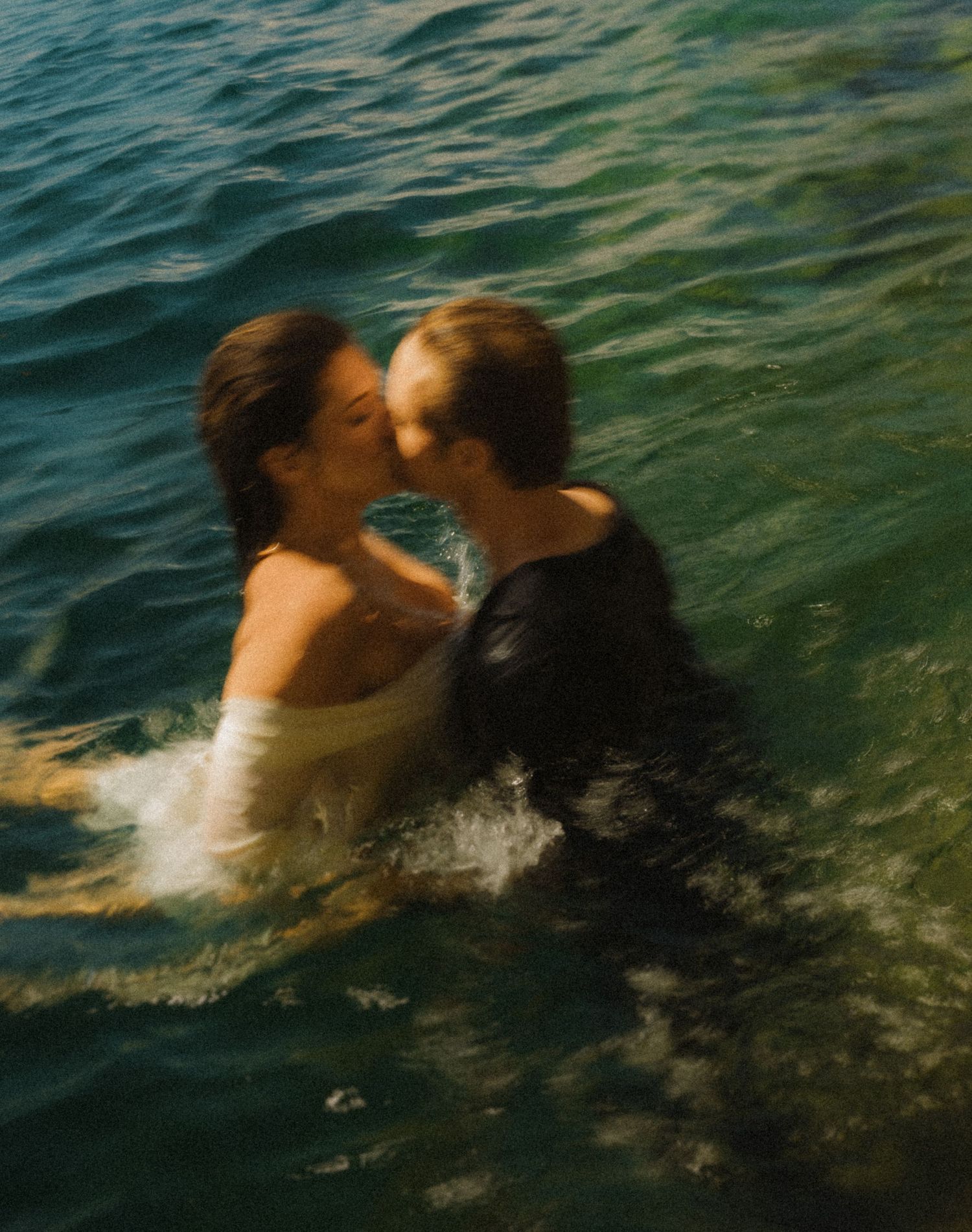 Couple sharing a romantic kiss while standing in turquoise ocean water during a swim.