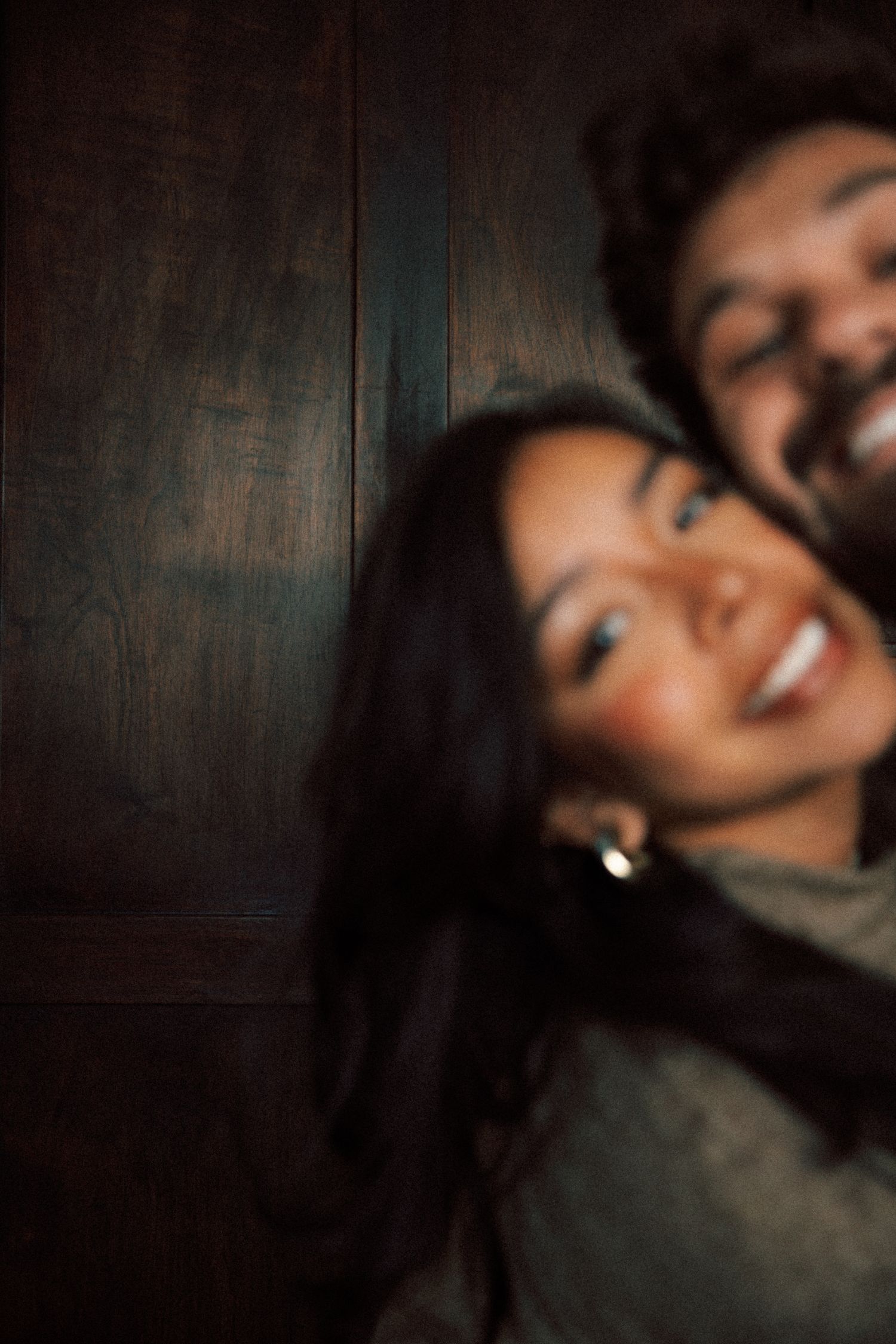 Blurred close-up of smiling couple laughing together against dark wooden wall background.