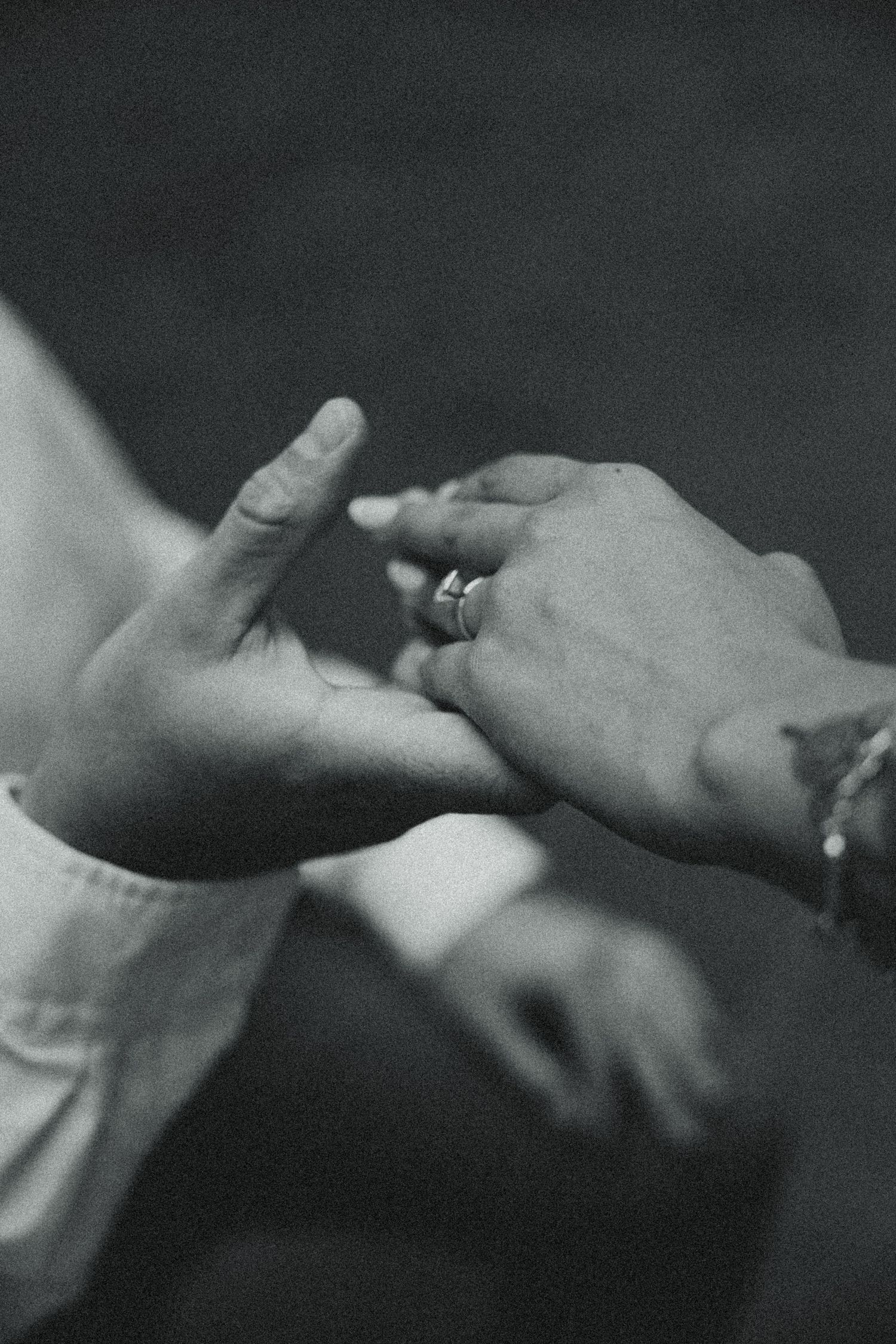 Black and white photo of a person placing a diamond ring on another persons finger during a wedding ceremony.