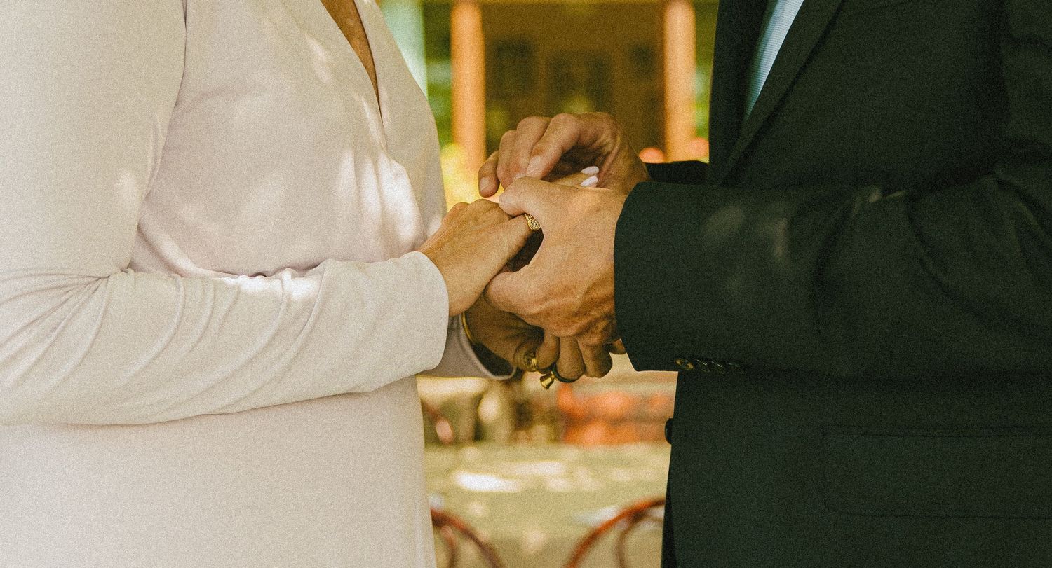 Couple exchanging wedding rings during ceremony, bride in white dress and groom in dark suit.