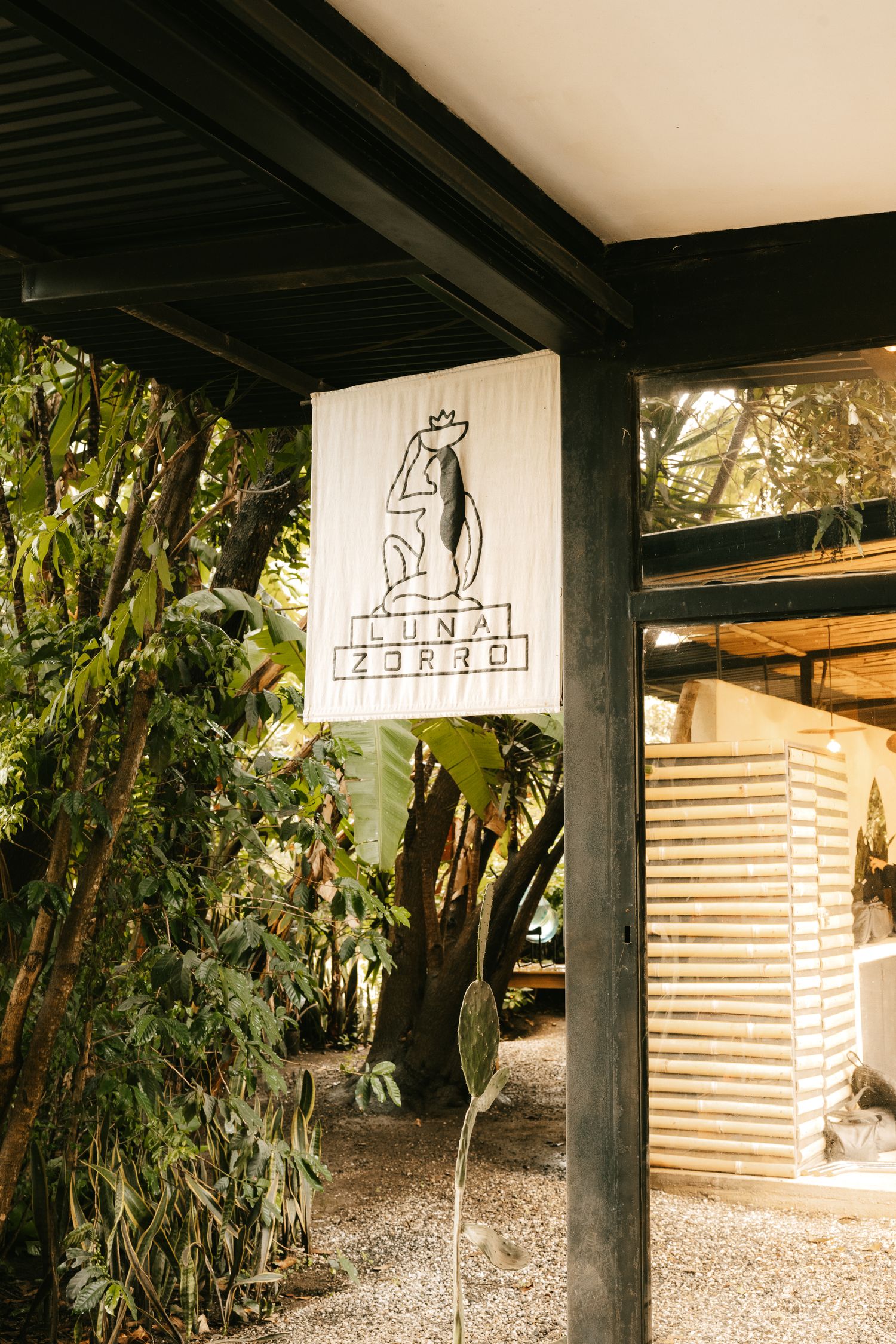 Outdoor sign for Nina Zorro restaurant surrounded by lush tropical greenery and modern architecture.