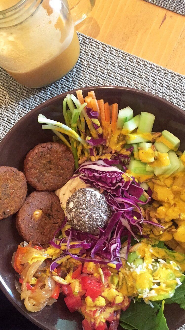 Colorful vegan Buddha bowl with falafel, red cabbage, carrots, cucumber, turmeric rice, and creamy dressing on the side.
