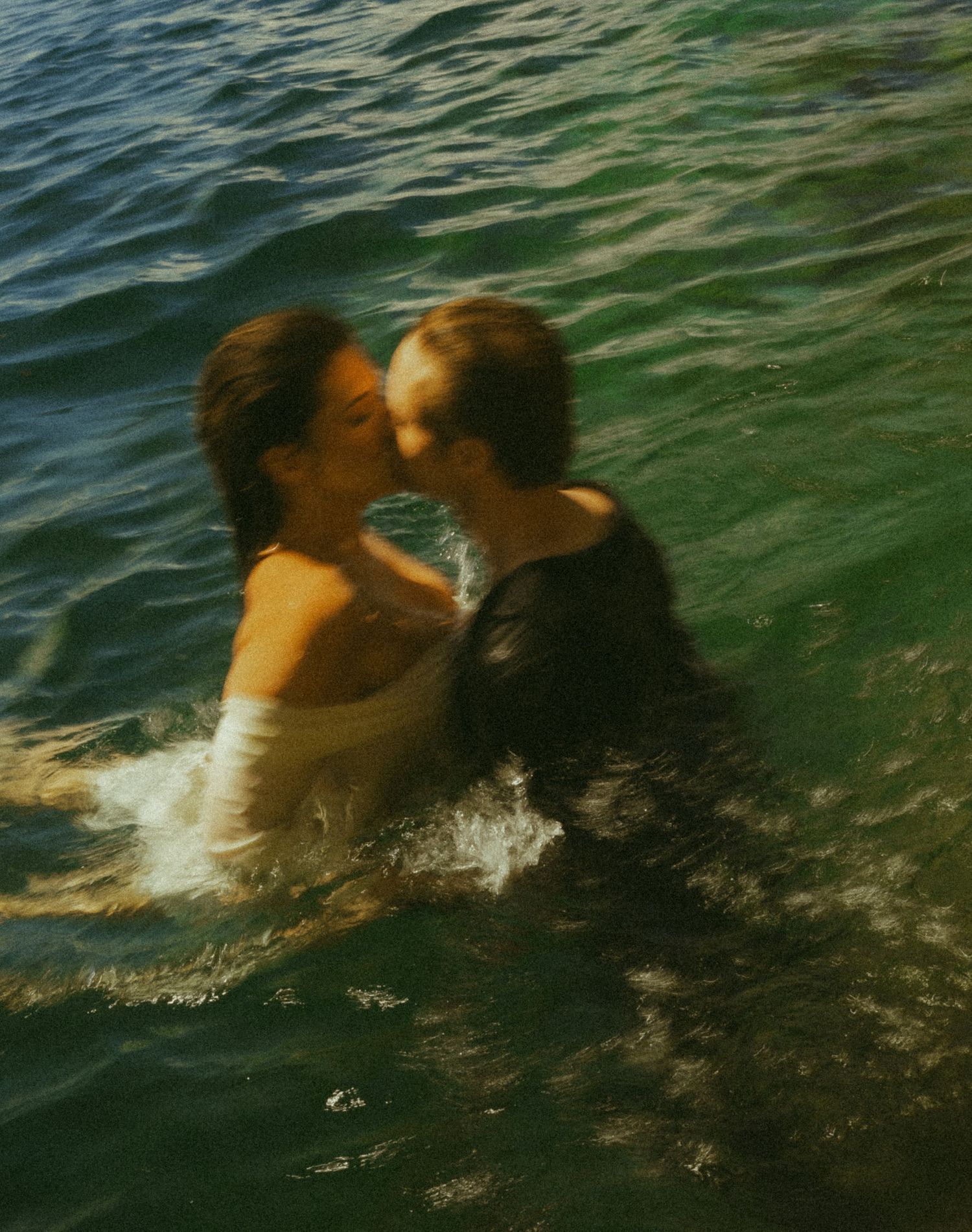 Couple kissing while submerged in sparkling green lake water during wedding photo session.