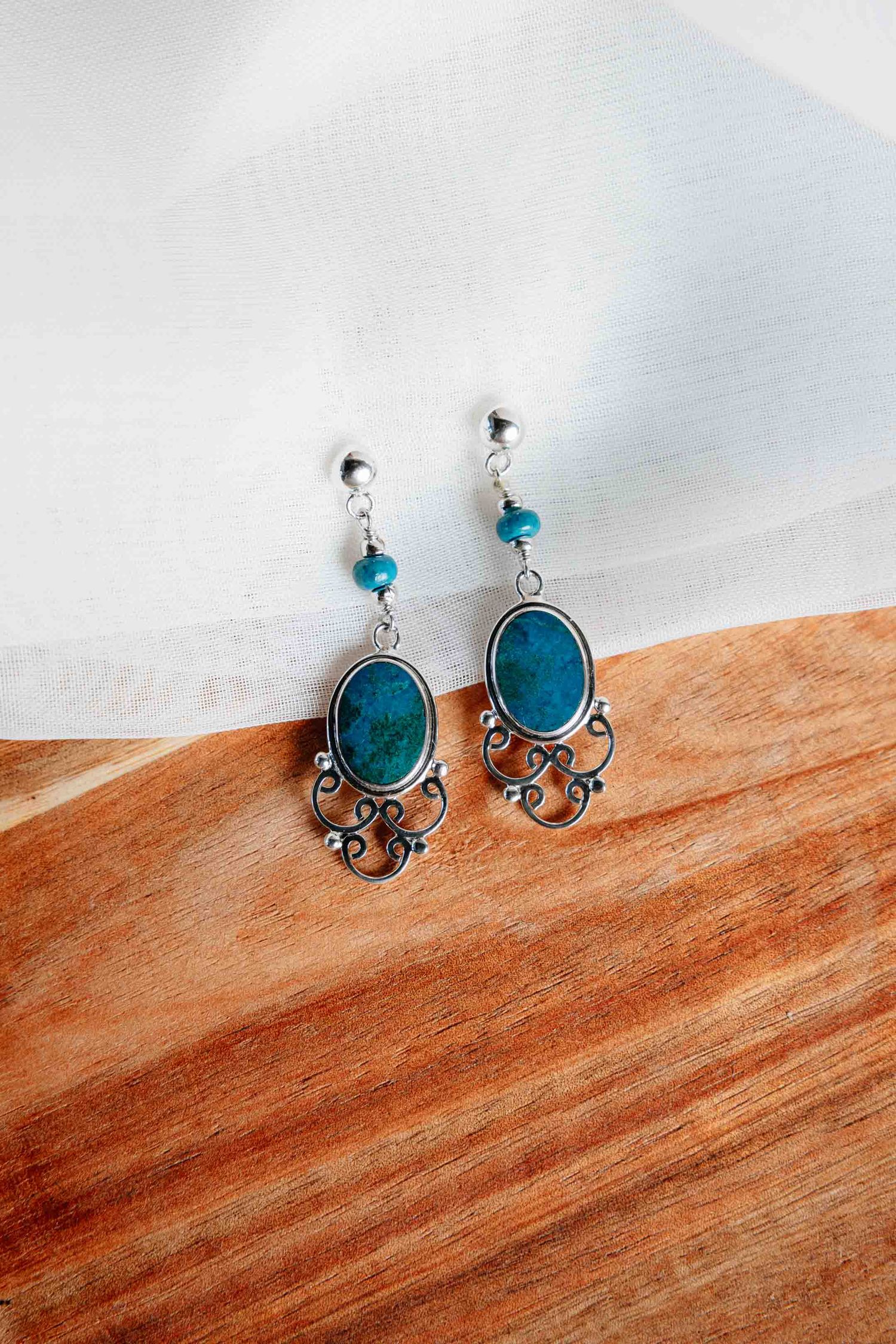 Silver filigree drop earrings featuring oval turquoise stones and small beads on wood surface.