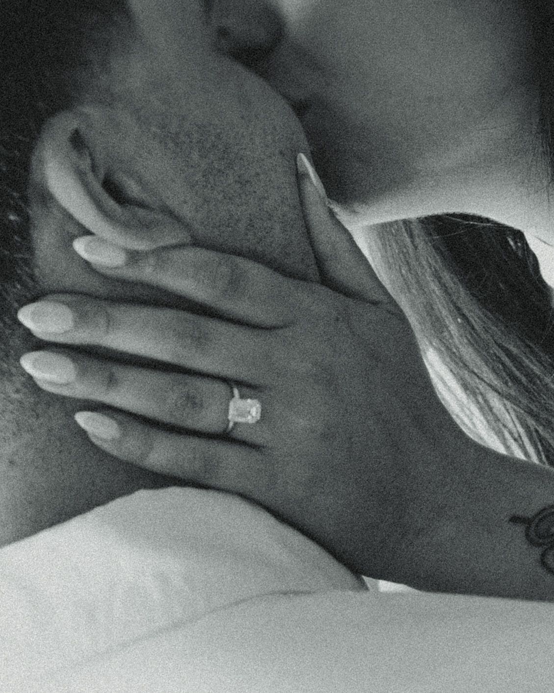 Black and white photo of a couple embracing, featuring a sparkling diamond engagement ring on the womans hand.