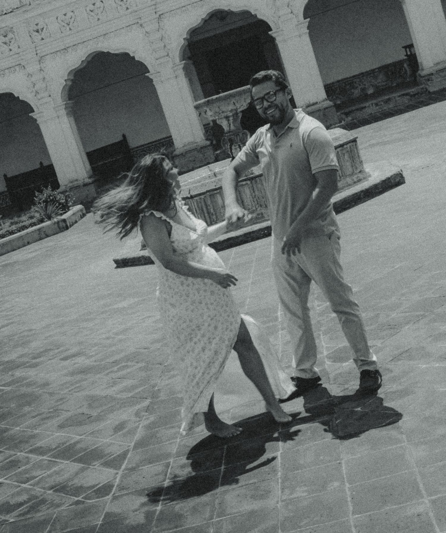 A couple dancing joyfully in a historic courtyard, captured in black and white photography.