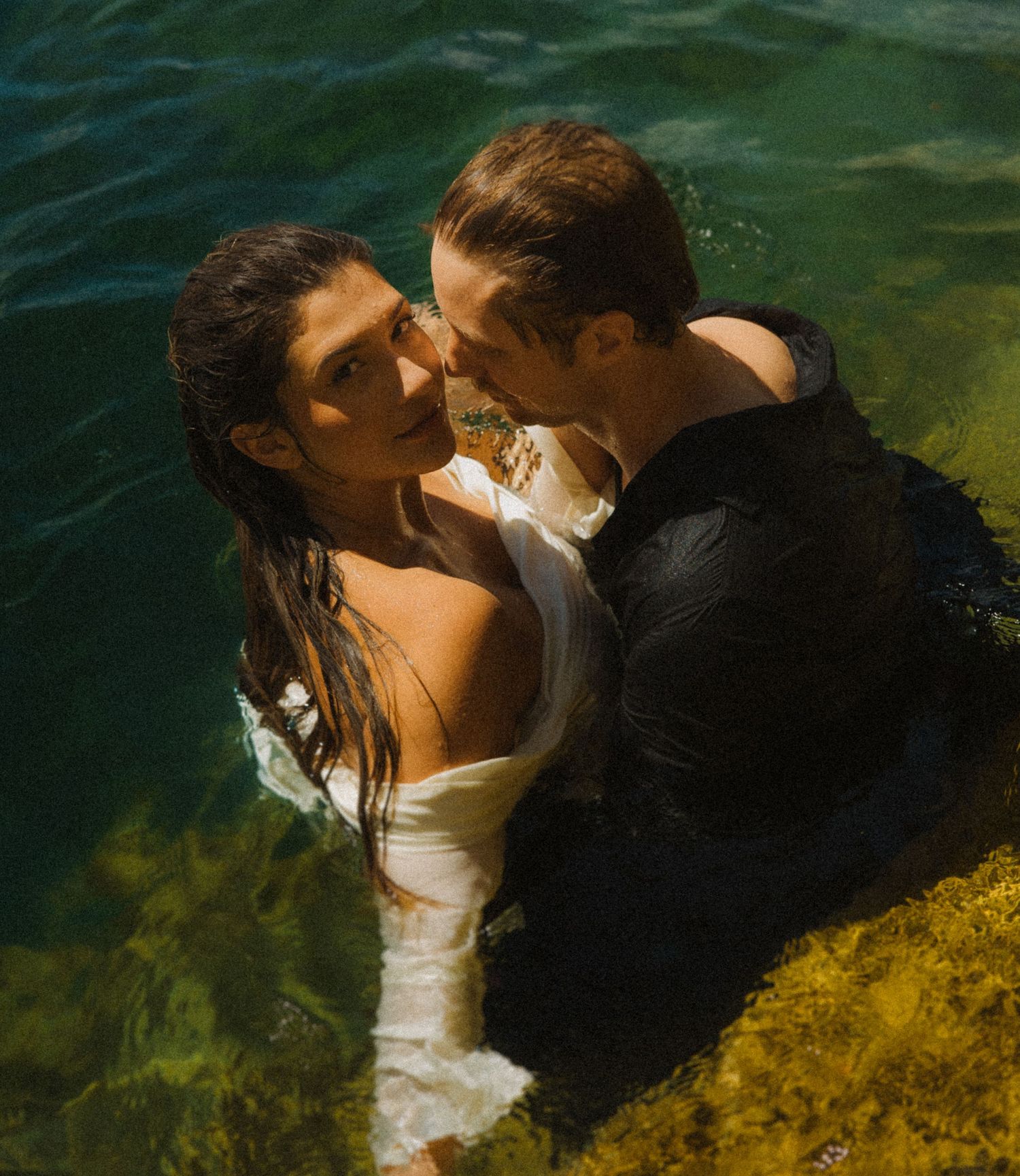 Bride and groom share a romantic kiss while wading in crystal clear turquoise water.