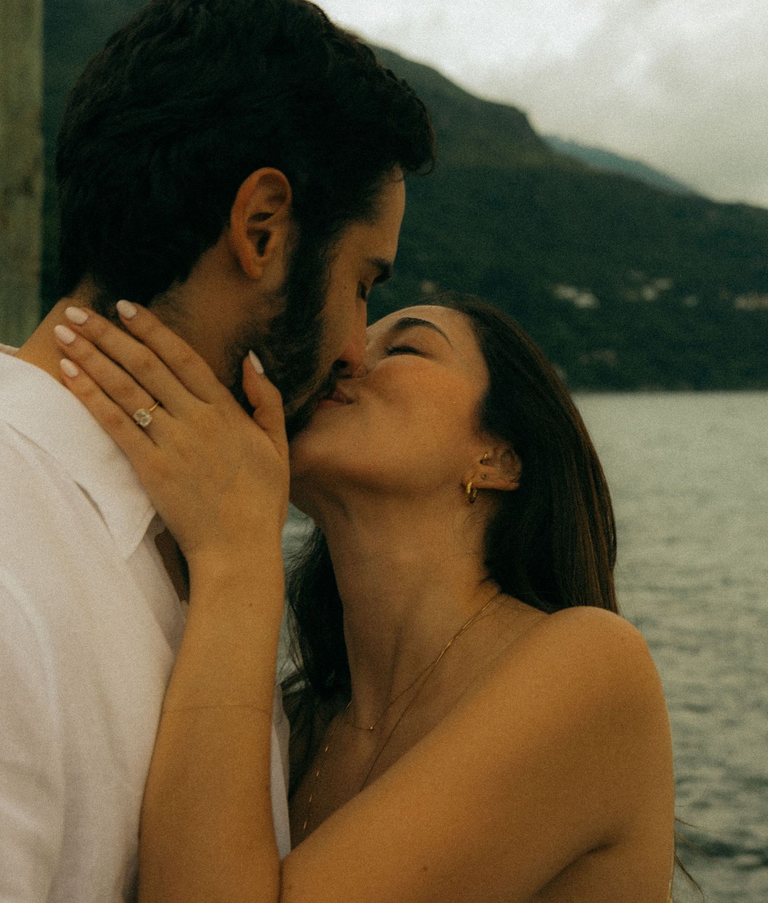 Romantic couple sharing a tender kiss outdoors with a scenic mountain lake backdrop.