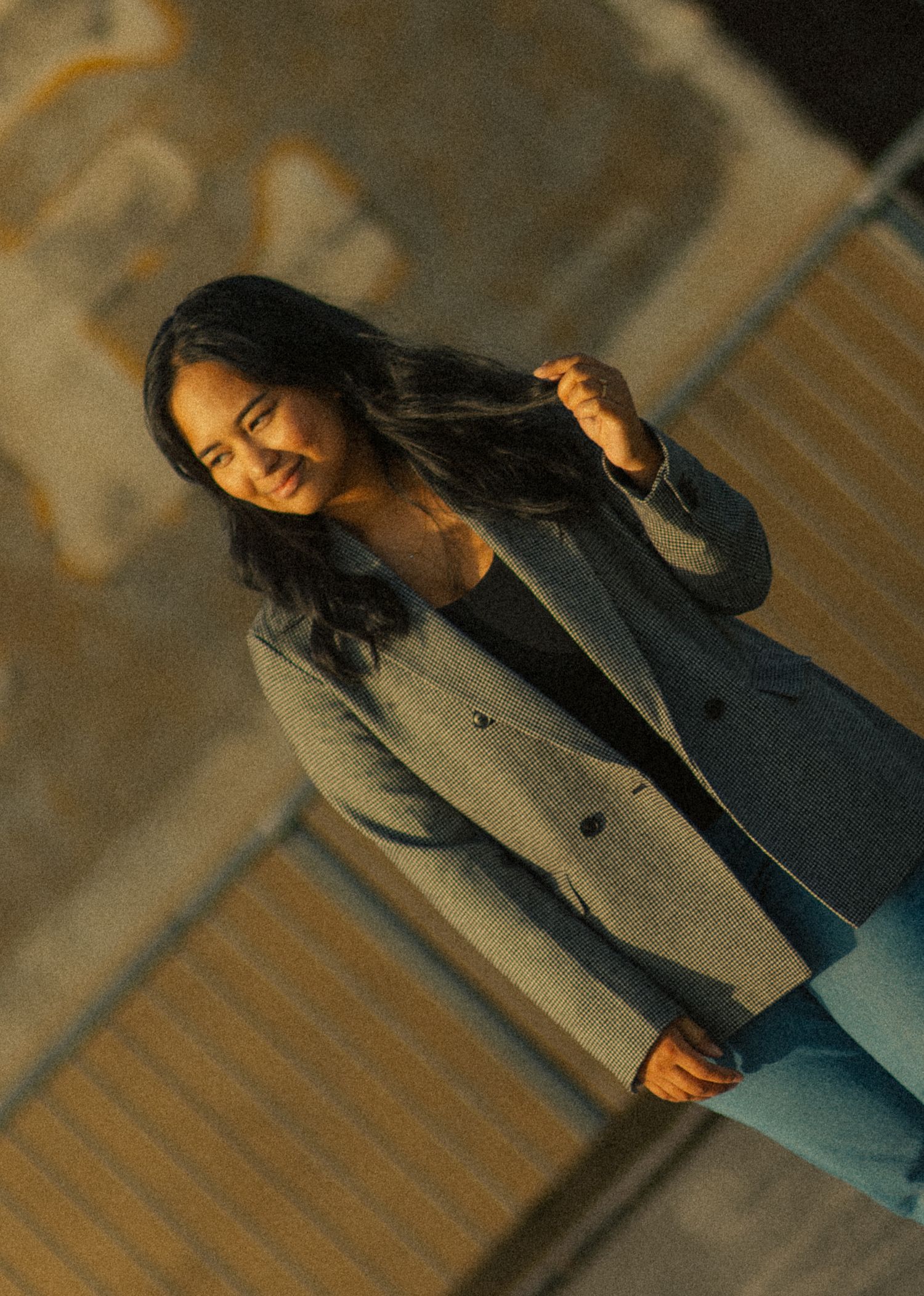 Young woman in gray blazer and blue jeans smiling outdoors in warm evening light.