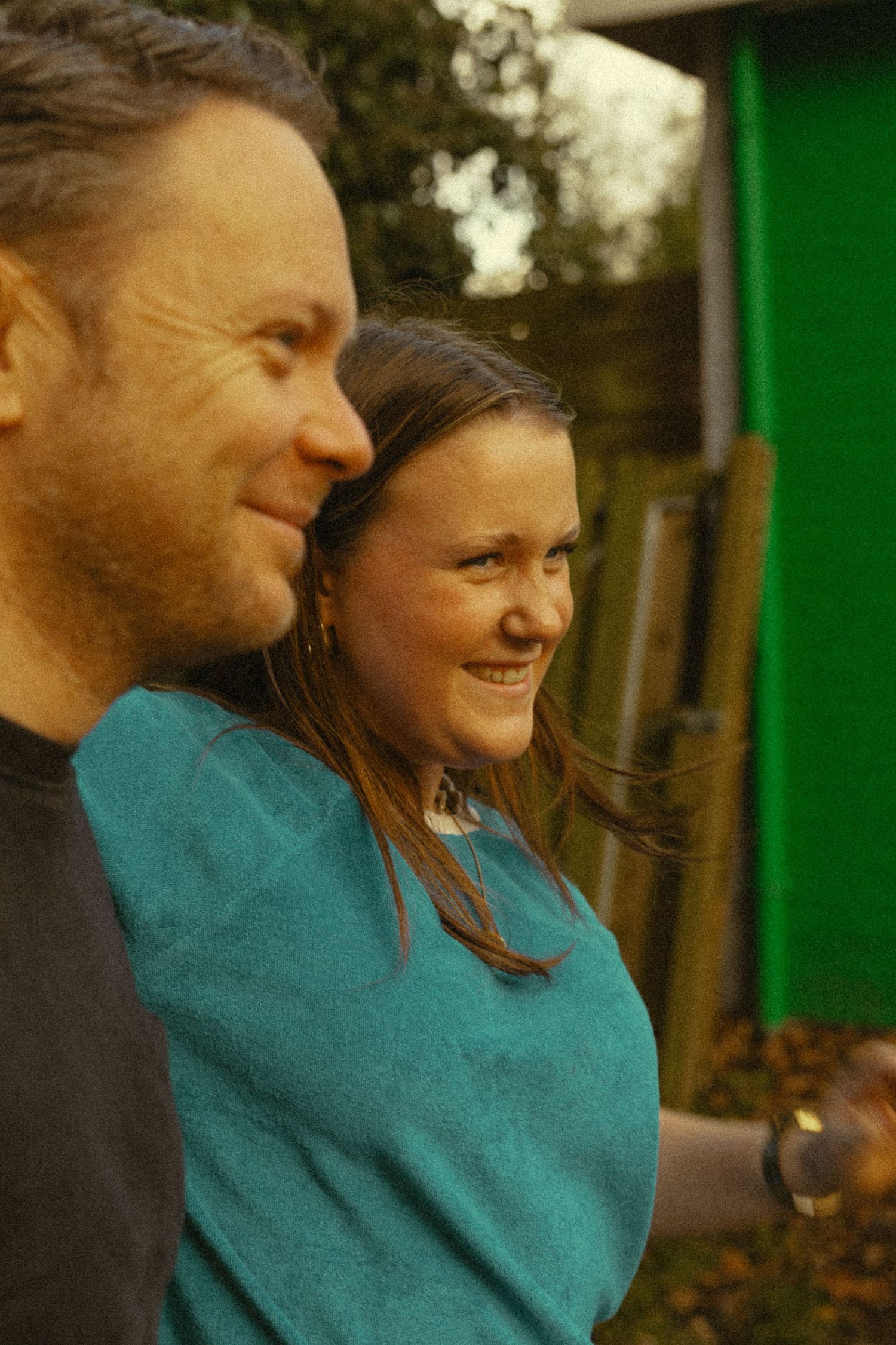 A man and woman smiling outdoors near a green building, captured in a warm, candid portrait photo.