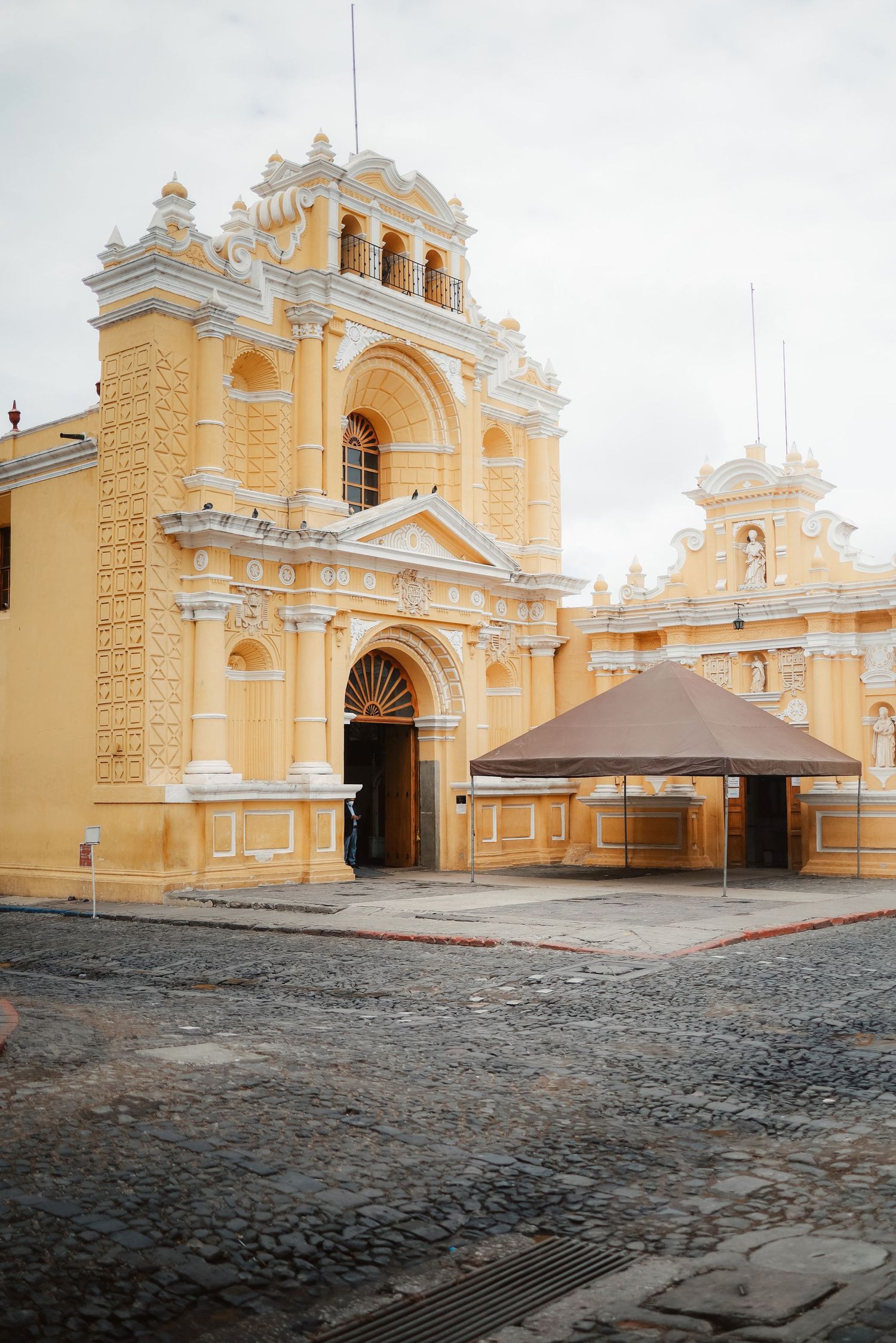 Yellow colonial church with ornate white facade and cobblestone street in Antigua, Guatemala.