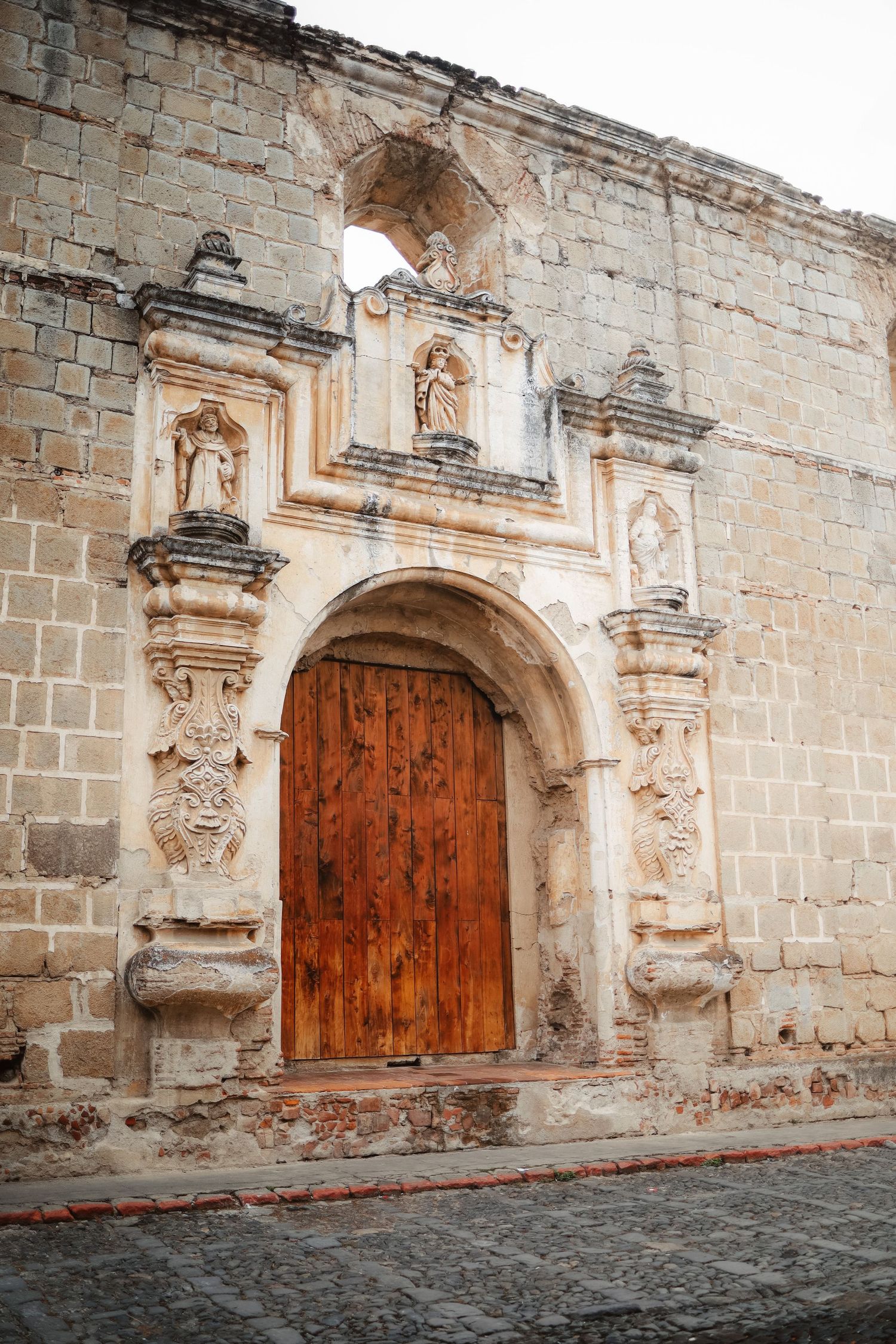 Historic colonial stone church facade with ornate carved archway and wooden door in Antigua, Guatemala.