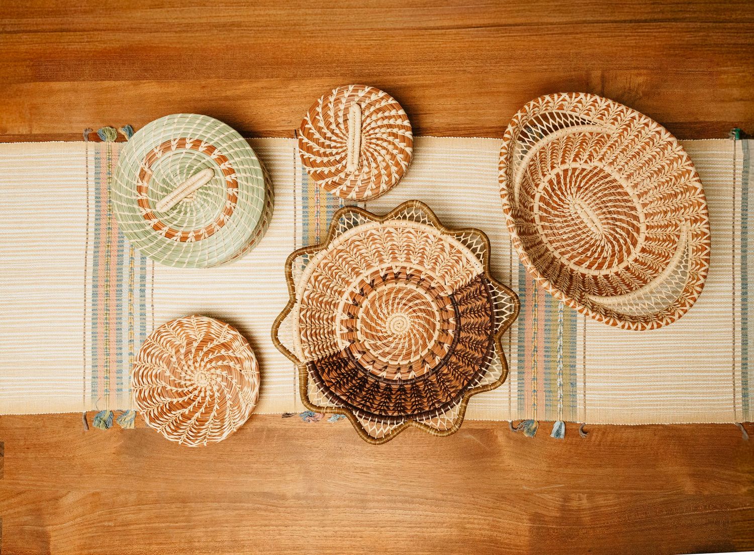 Assorted woven seagrass baskets arranged flat on a striped table runner on a wooden surface.