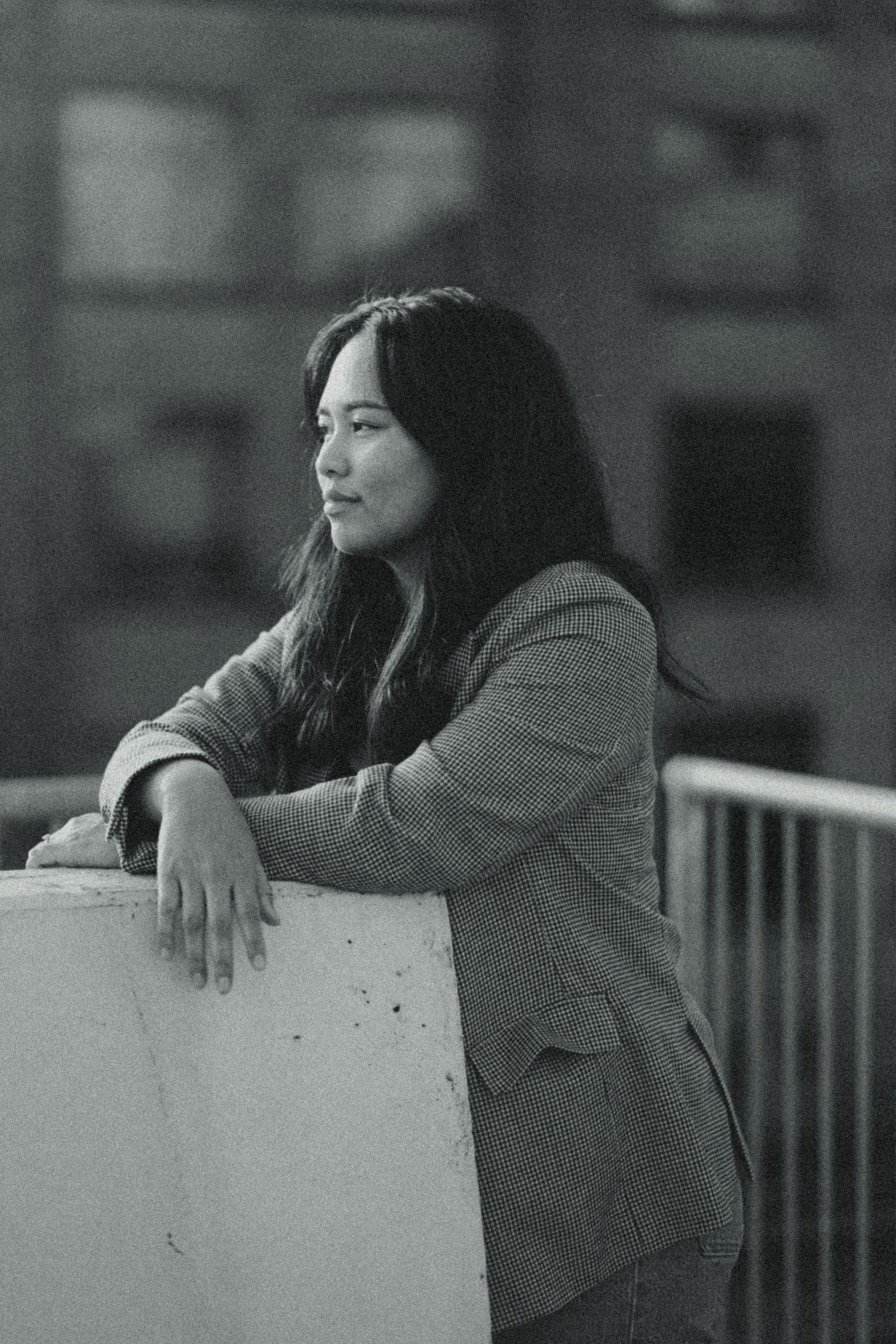 Black and white portrait of a young woman with long hair leaning on a ledge outdoors, wearing a blazer.
