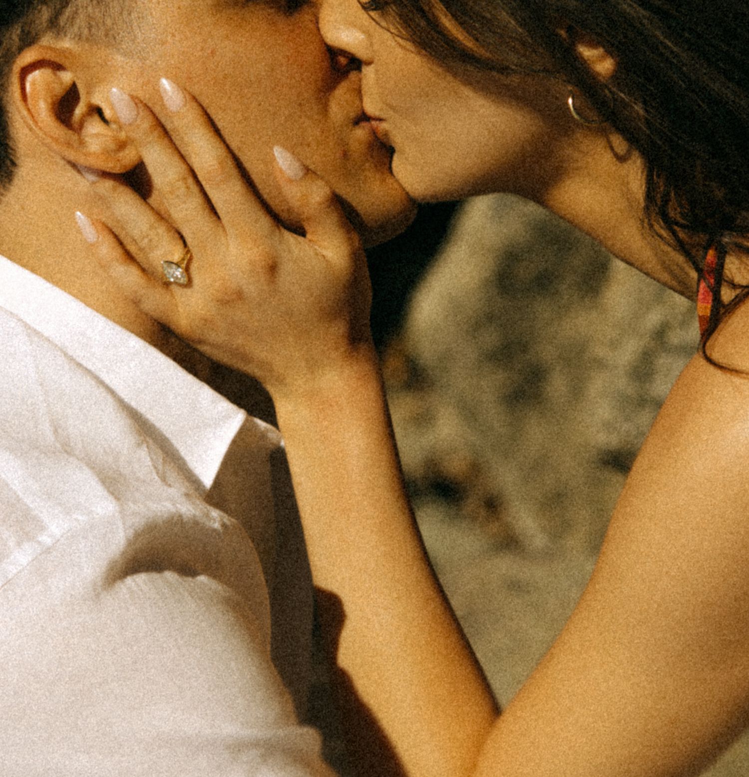 Couple sharing a romantic kiss, woman wearing a gold ring, close-up shot with soft natural lighting.