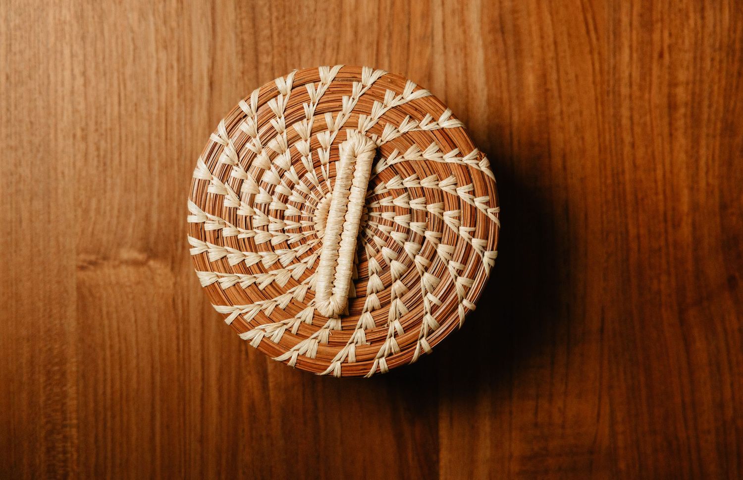 Top view of a round handwoven natural fiber basket with lid on wooden surface.
