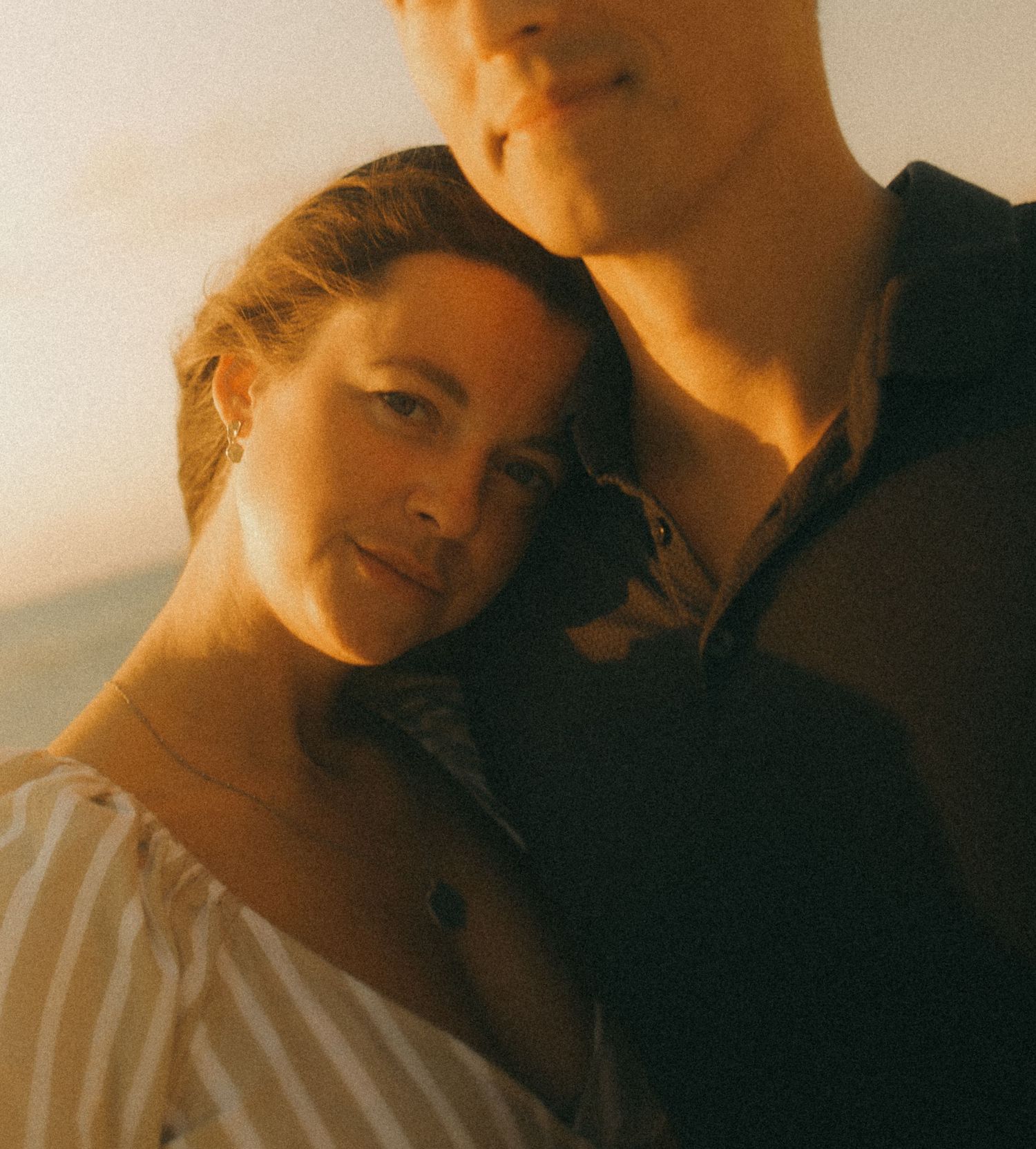 A couple shares a tender moment at golden hour, woman resting her head on a man's shoulder outdoors.